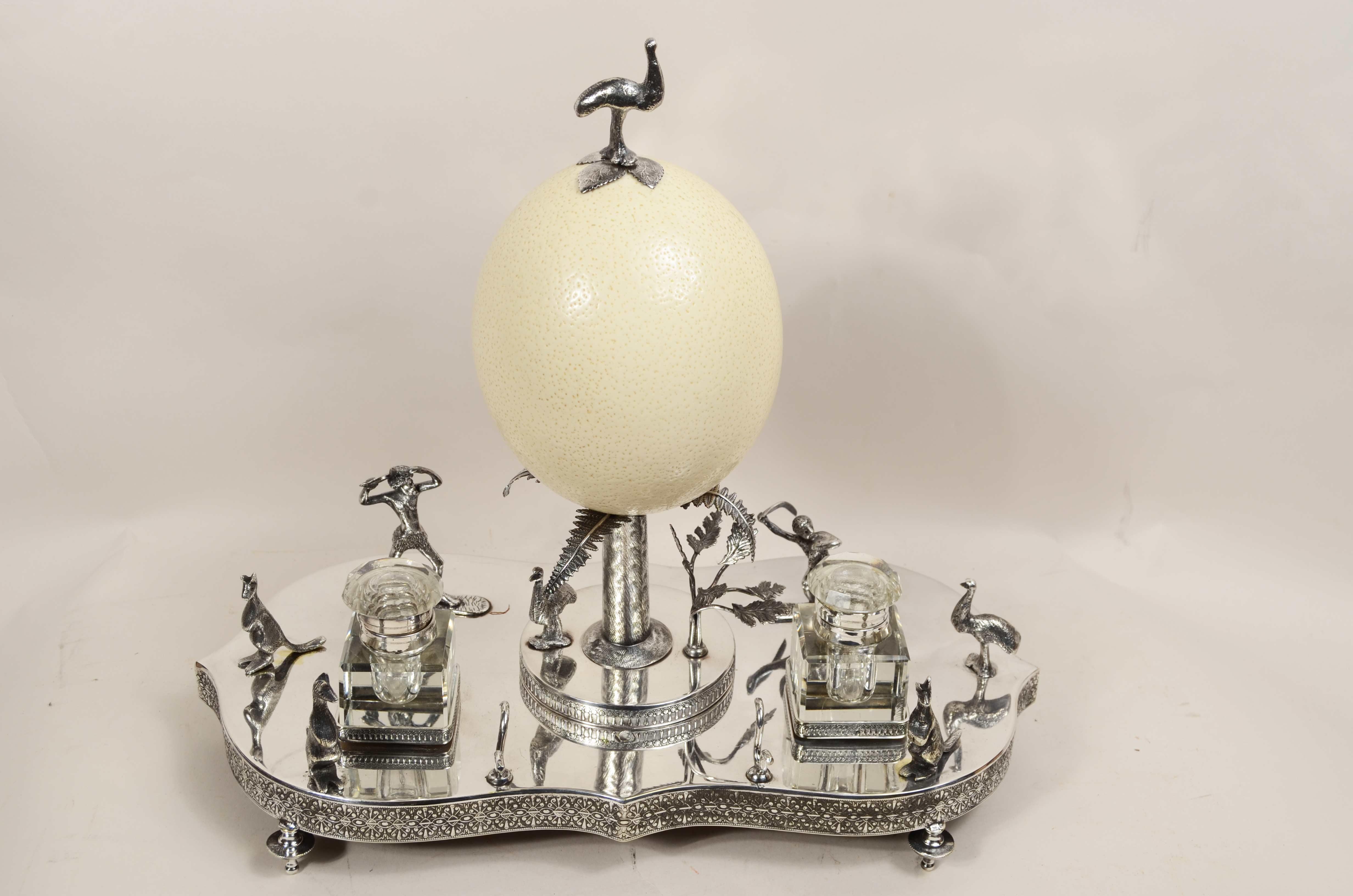 Victorian-era silver plate wunderkammer inkwell that  presents  in the center of the tray a palm tree from the  cut trunk on which rests reclining on four palm leaves an Australian emu egg surmounted in turn by a silver-plated metal casting emu. On