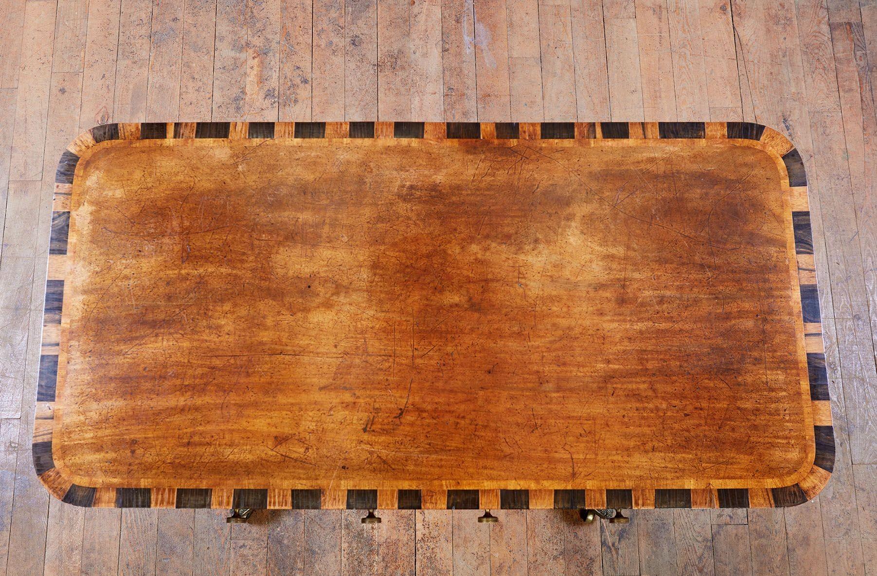 Mesa de sofá inglesa con tablero rectangular de esquinas redondeadas en rara madera de calamandro e incrustaciones de calamandro y ébano en los bordes, sobre delantal frontal con volutas y flores de bronce dorado y dos cajones con molduras de ébano