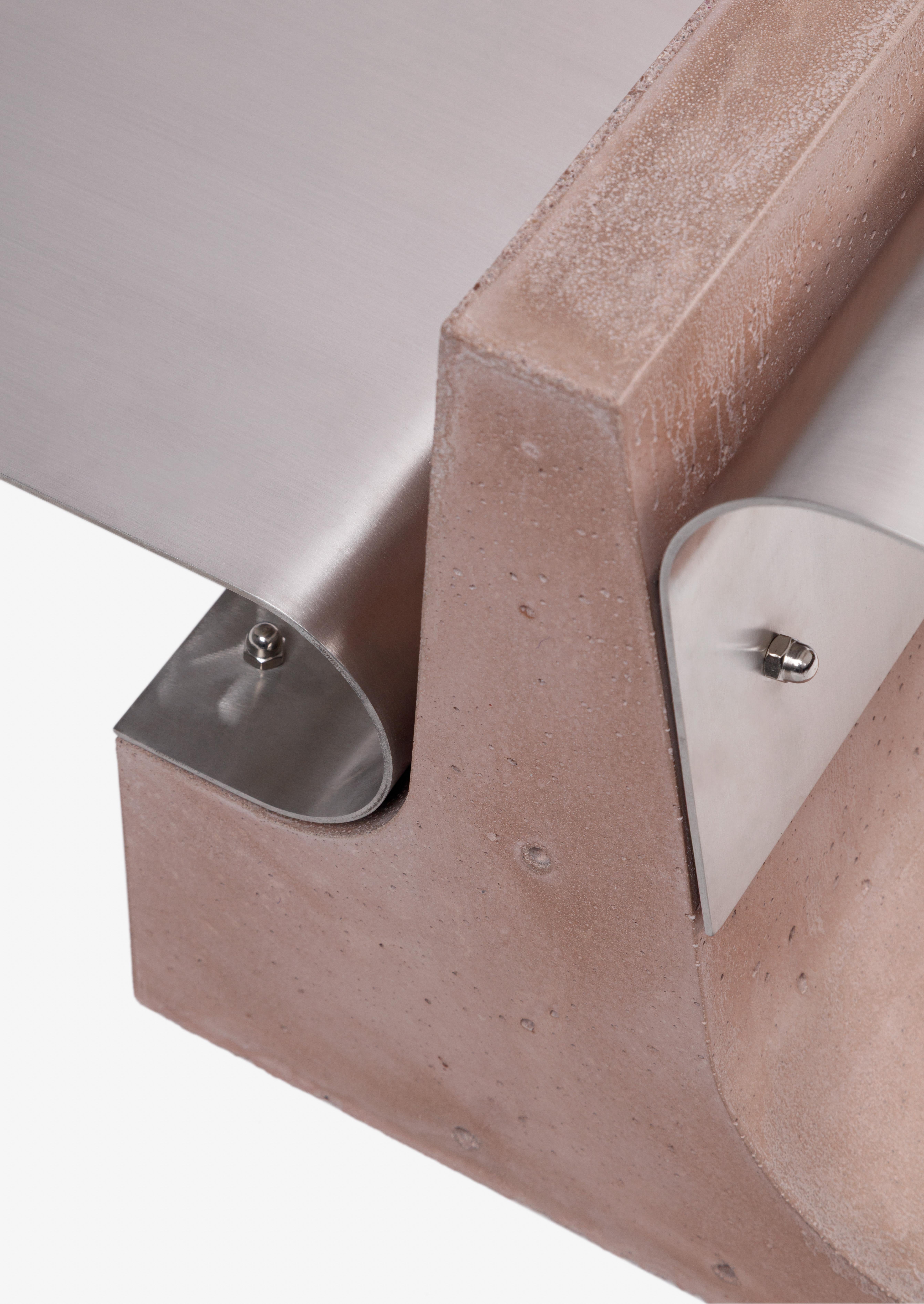 Une base de béton rosé contraste avec un élément en acier biseauté, créant une composition nettement définie qui équilibre le poids et la légèreté, l'immobilité et le mouvement. L'œuvre reflète la capacité de Simões à transformer la logique de