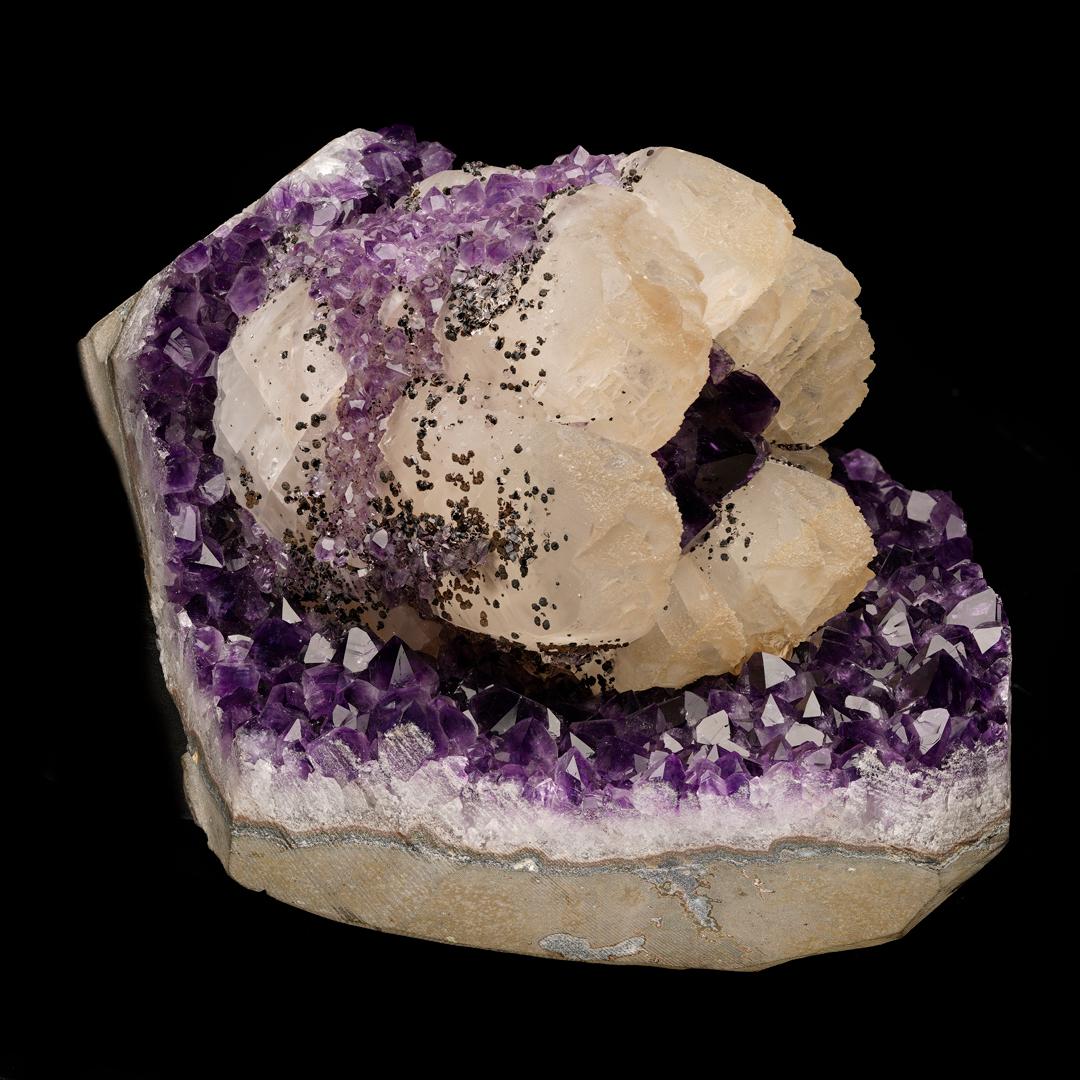 This floral arrangement features waxy pale yellow calcite with a scattering of glimmering black goethite crystals resting on a bed of deep purple Uruguayan amethyst with a second generation of amethyst in the center of and overflowing onto the sides