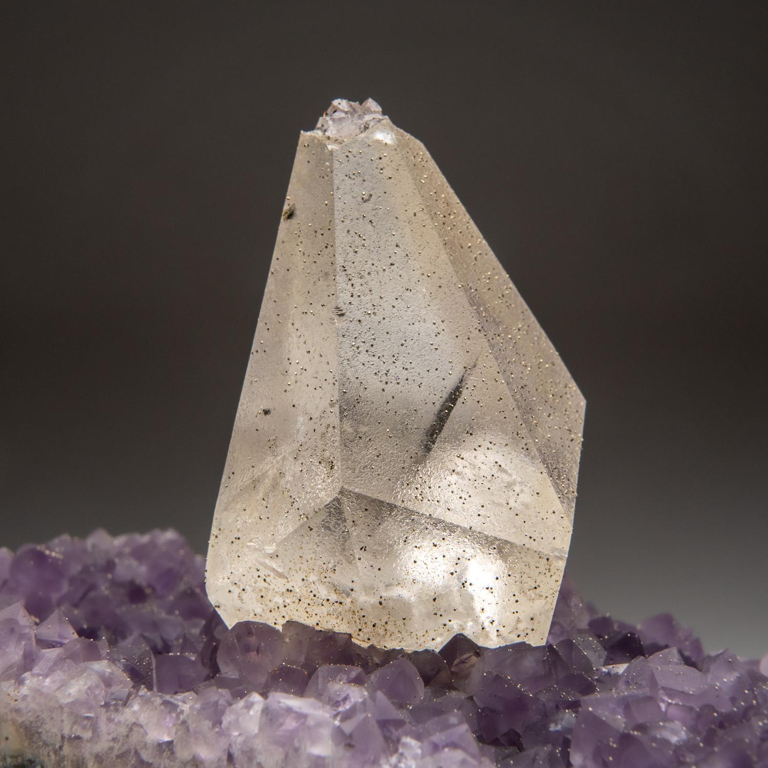 From San Eugenio, Artigas Dept., Uruguay

Large 5'' scalenohedral crystal of calcite with pyrite on amethyst matrix accented by isolated cluster of colorless quartz. The calcite crystal shows fully terminated faces composed of small micro etched