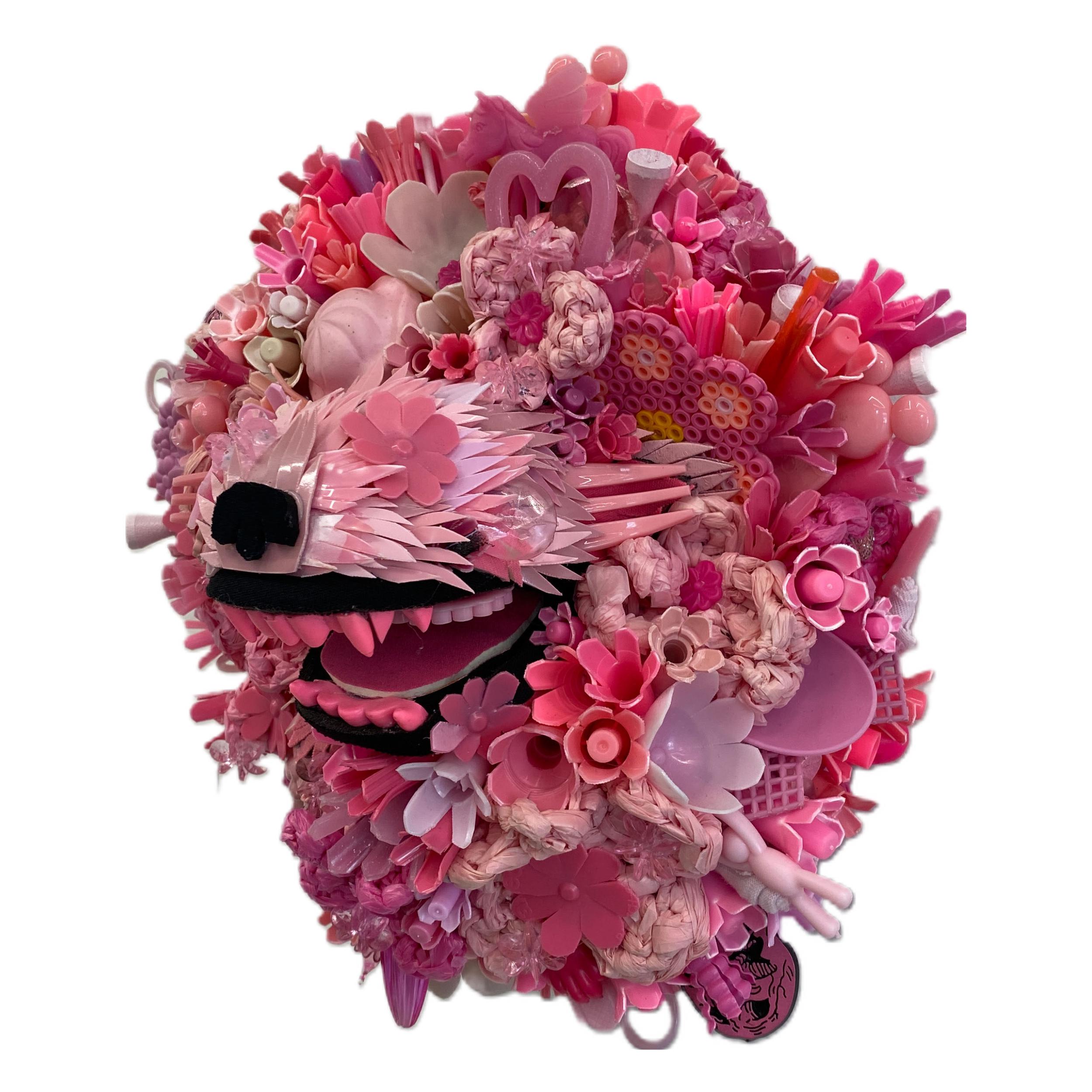 A 2021 sculpture by Calder Kamin, measuring  10 inches tall, 9 inches wide, and 6 inches deep. Hydrangea Hound IV is made up of recycled materials including plastic bags, koozies, caps, cutlery, plastic eggs, plastic containers, bottle caps, marker