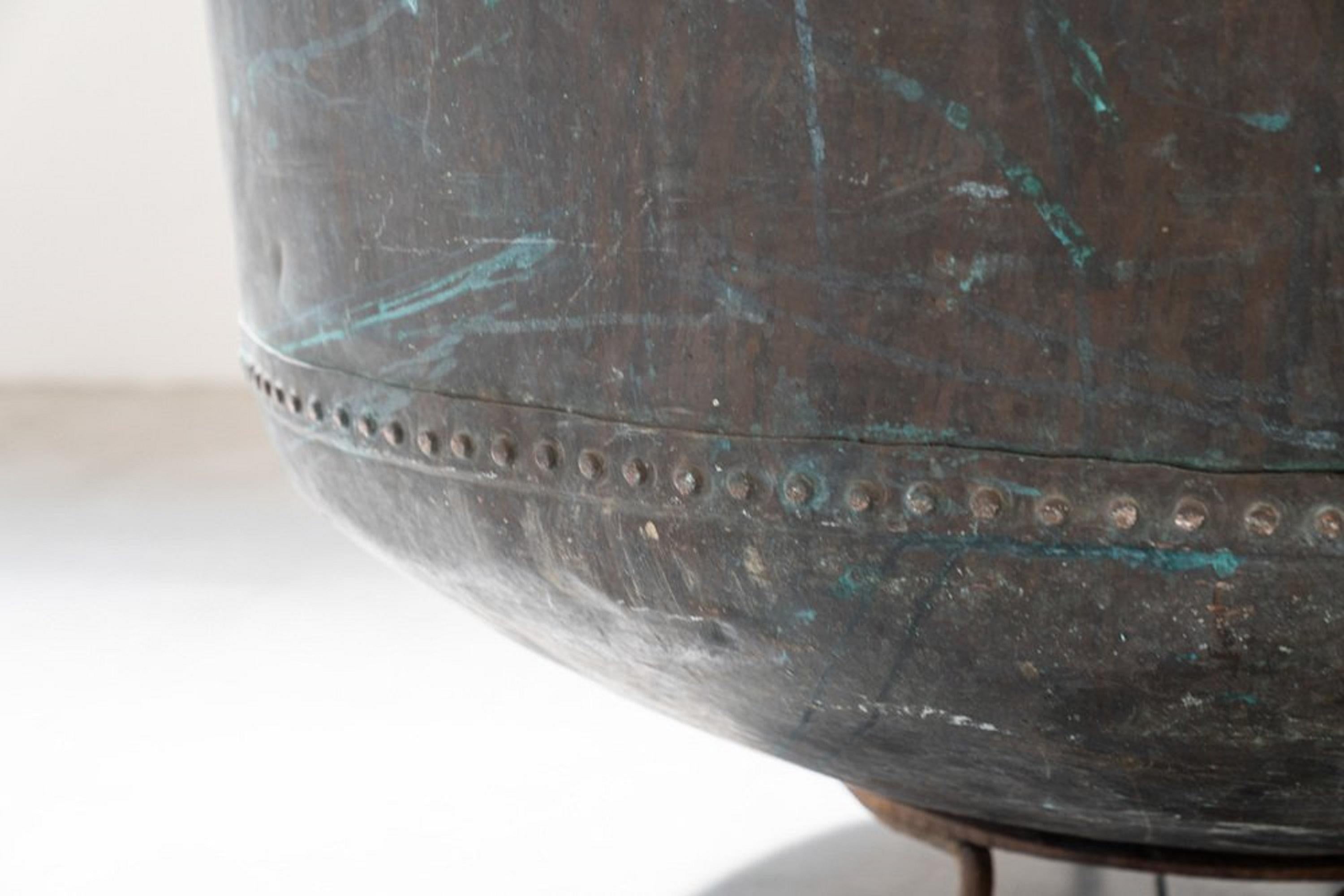 Questo magnifico calderone antico in rame, risalente all'inizio del XIX secolo, è un pezzo di storia che cattura l'essenza dell'artigianato tradizionale. La sua imponente struttura poggia su una solida base in ferro a treppiede, che ne garantisce la