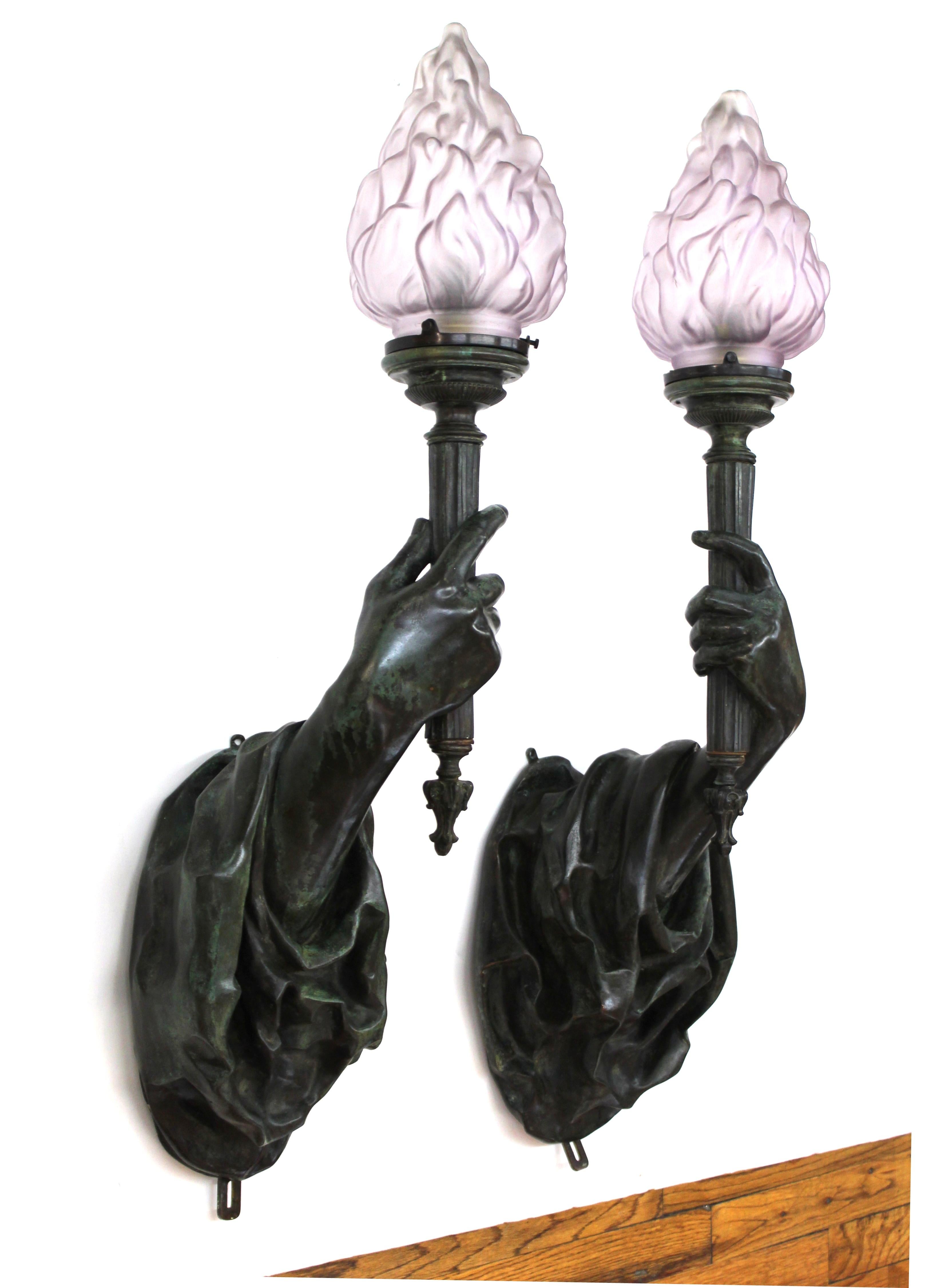 American Gilded Age or Belle Époque pair of heavy patinated cast bronze hand torchiere wall sconces, attributed to Edward F. Caldwell & Co. in New York City. The pair of sconces has elaborate drapery from which life-sized hands emerge, holding up