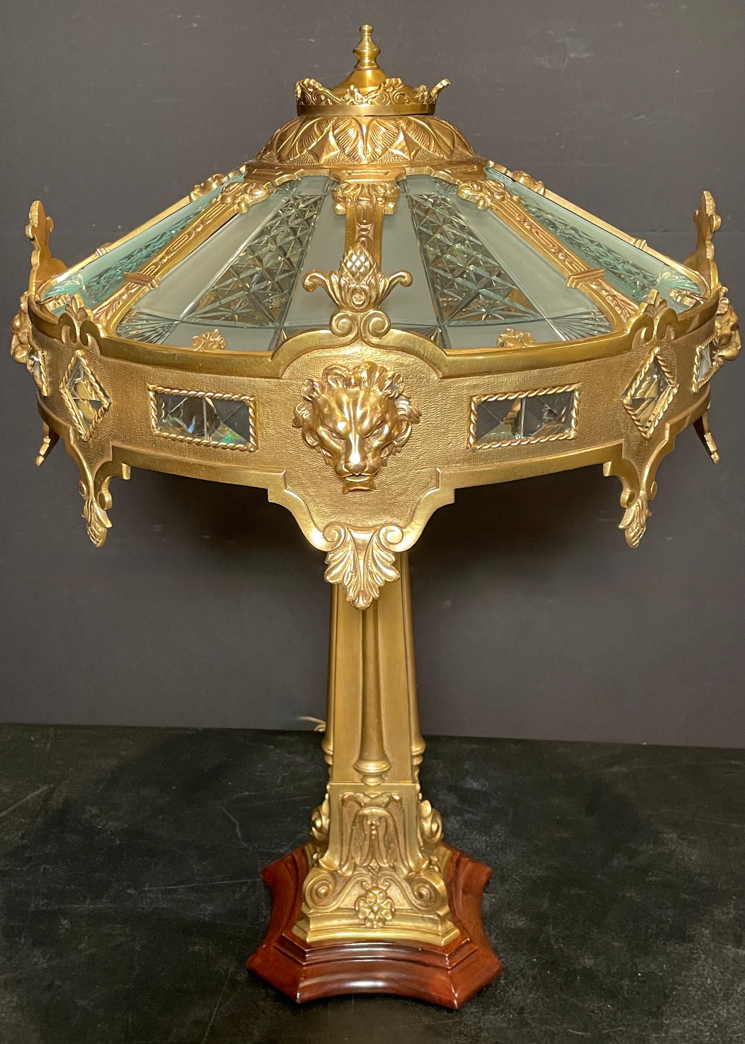 Caldwell bronze lamp base and shade with wheel cut glass panels. Lion mask mounts with crystal jewel inserts. Clean neoclassical lines define this lamp. Bronze column ending in a mahogany base.