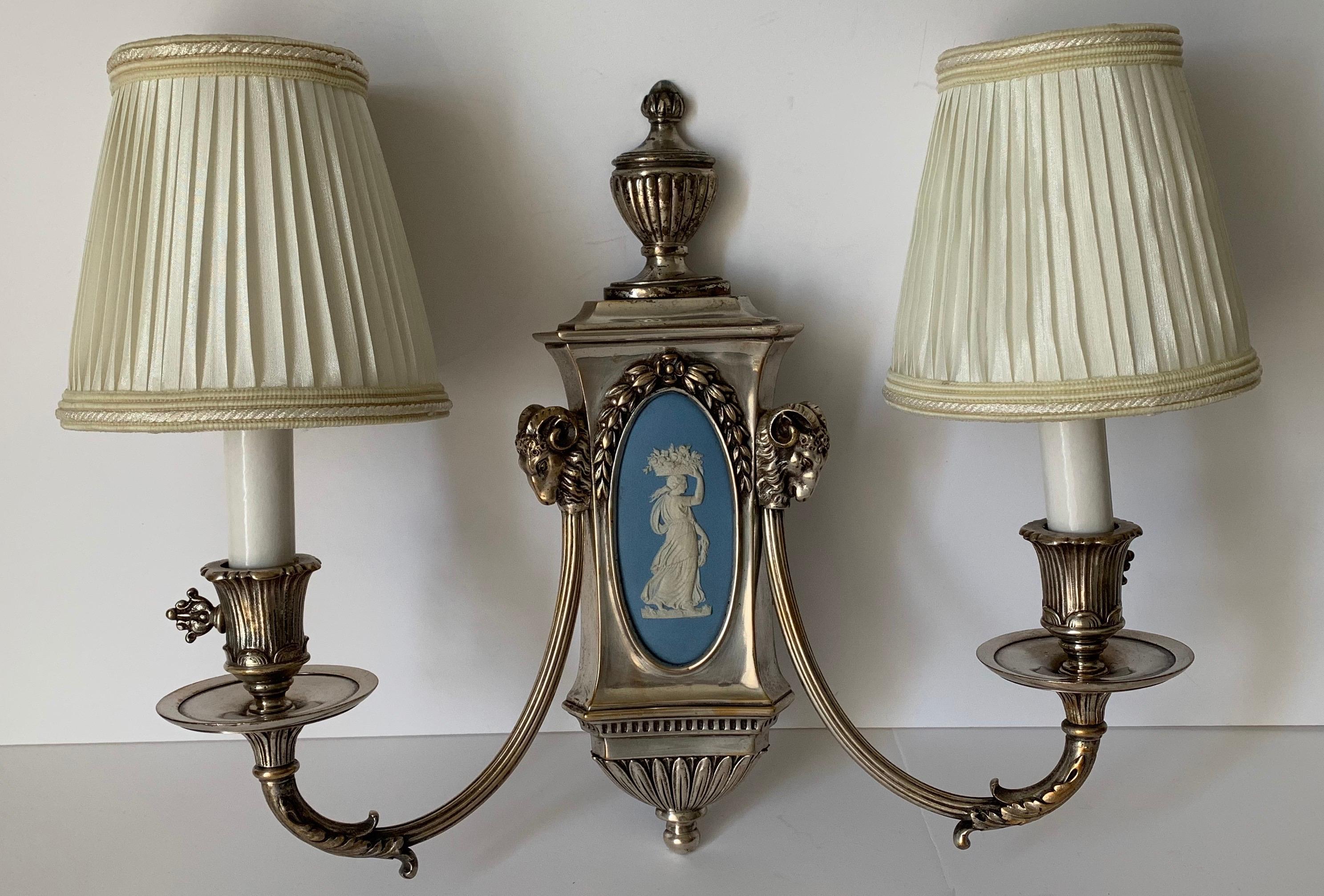 Pair of silver sconces by E.F. Caldwell. Wedgwood jasperware center plaques and silver plated bronze arms with urn and rams head detailing. Newly rewired. Each sconce takes two chandelier bulbs (not included). Ivory silk pleated lampshades are