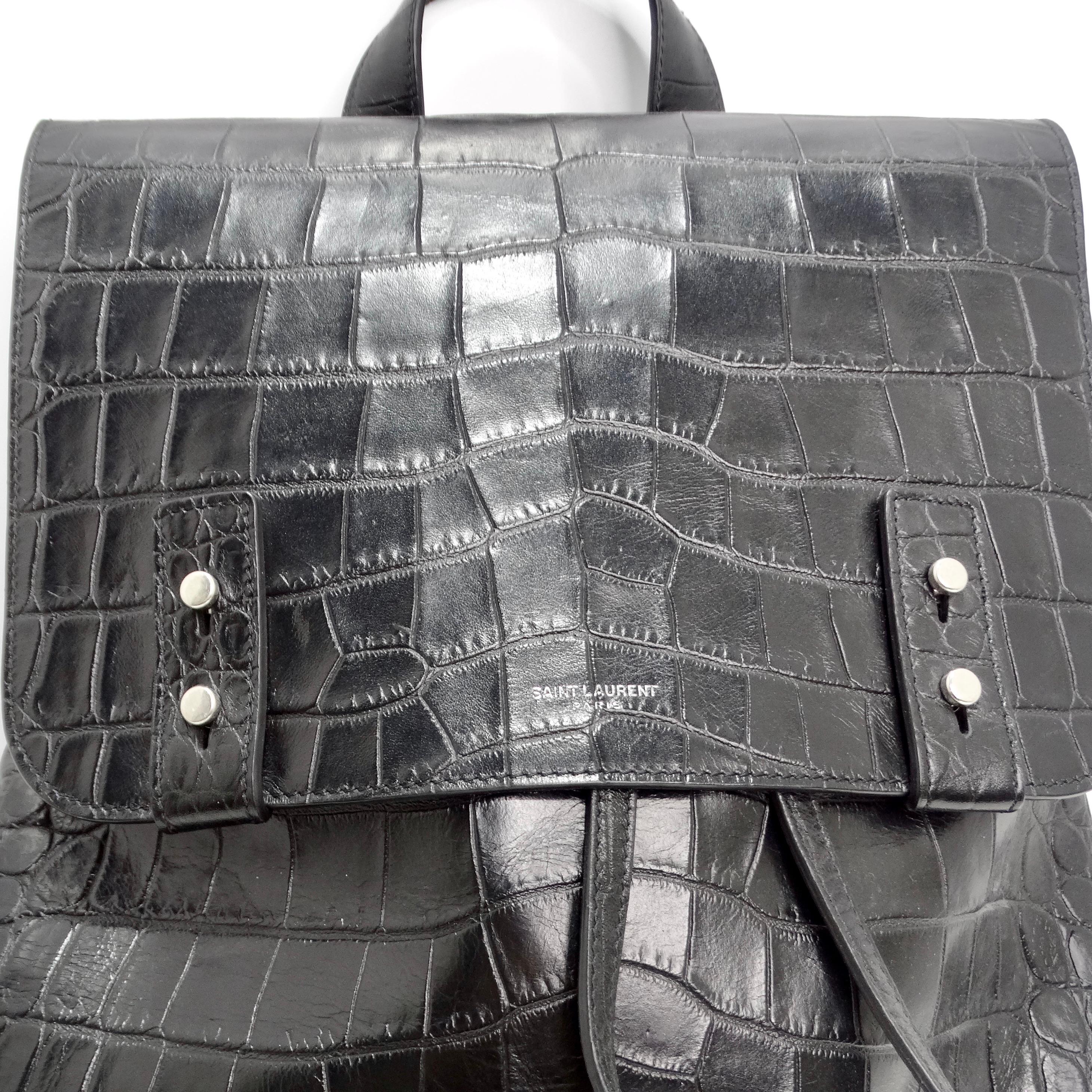 The Saint Laurent Calfskin Crocodile Embossed Sac De Jour Backpack in Black is an exquisite piece crafted from fine black crocodile-embossed calfskin leather, epitomizing luxury and sophistication. This backpack boasts a sleek and timeless design,