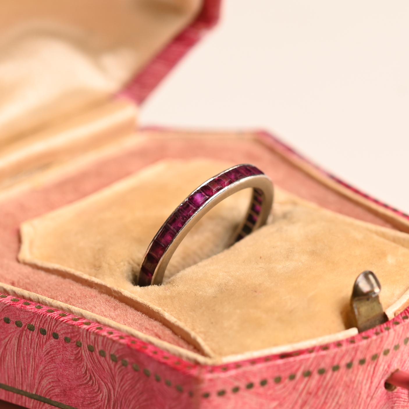 Cet exquis anneau d'éternité vintage présente un design intemporel, réalisé à la main dans un platine luxueux. Le bracelet présente une rangée ininterrompue de rubis vibrants taillés en calibre, sertis de manière experte dans un canal précis qui met