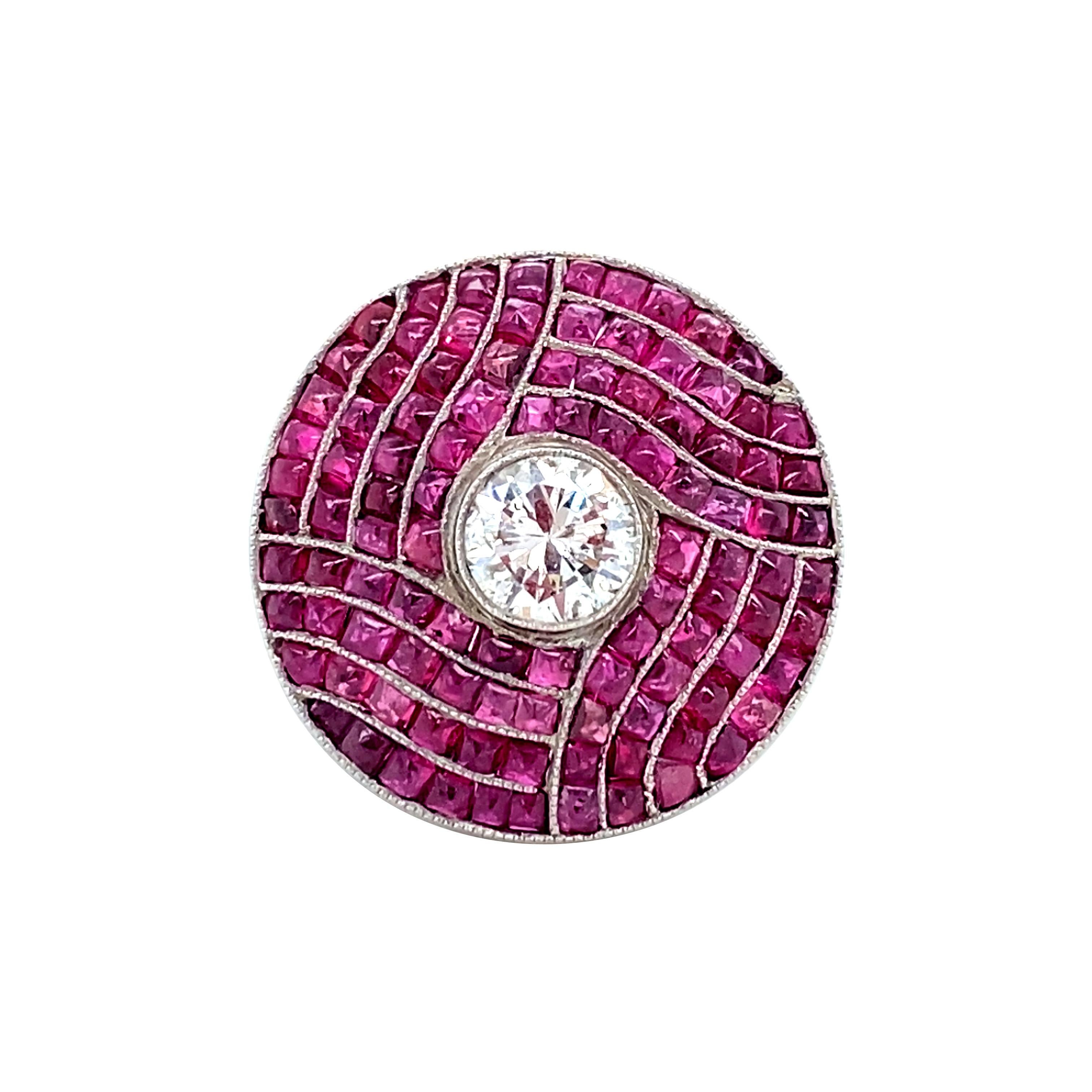 In the style of Art Deco, this ring features a central bezel-set 0.86 carat round brilliant cut diamond, surrounded by calibre cut natural rubies in a ring mount crafted entirely of precious platinum. An elegant under-gallery features graceful