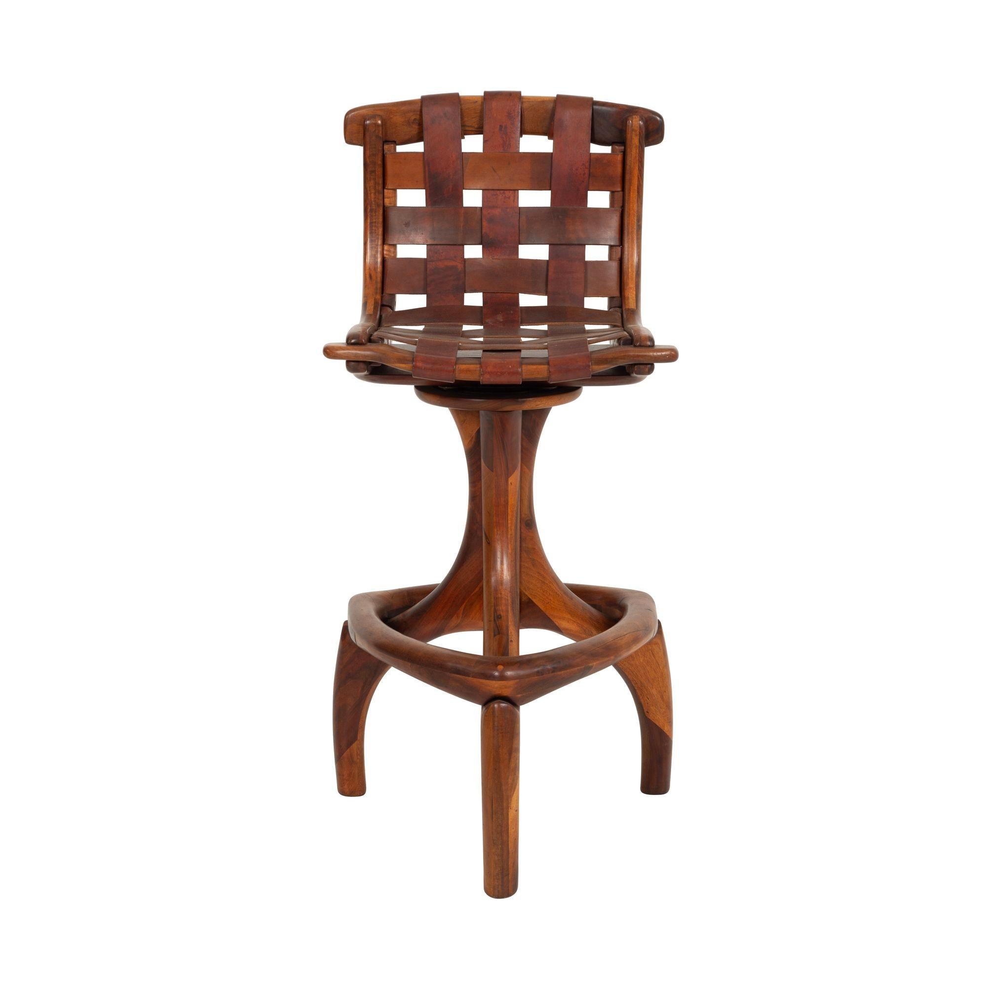 California Craft Arthur Espenet Carpenter Three Leg Counter Stool in Walnut Features original woven leather slung seat with sculpted wood L-shape frame. The stool has a 360 degree swivel mechanism master craftsman's and is supported by three