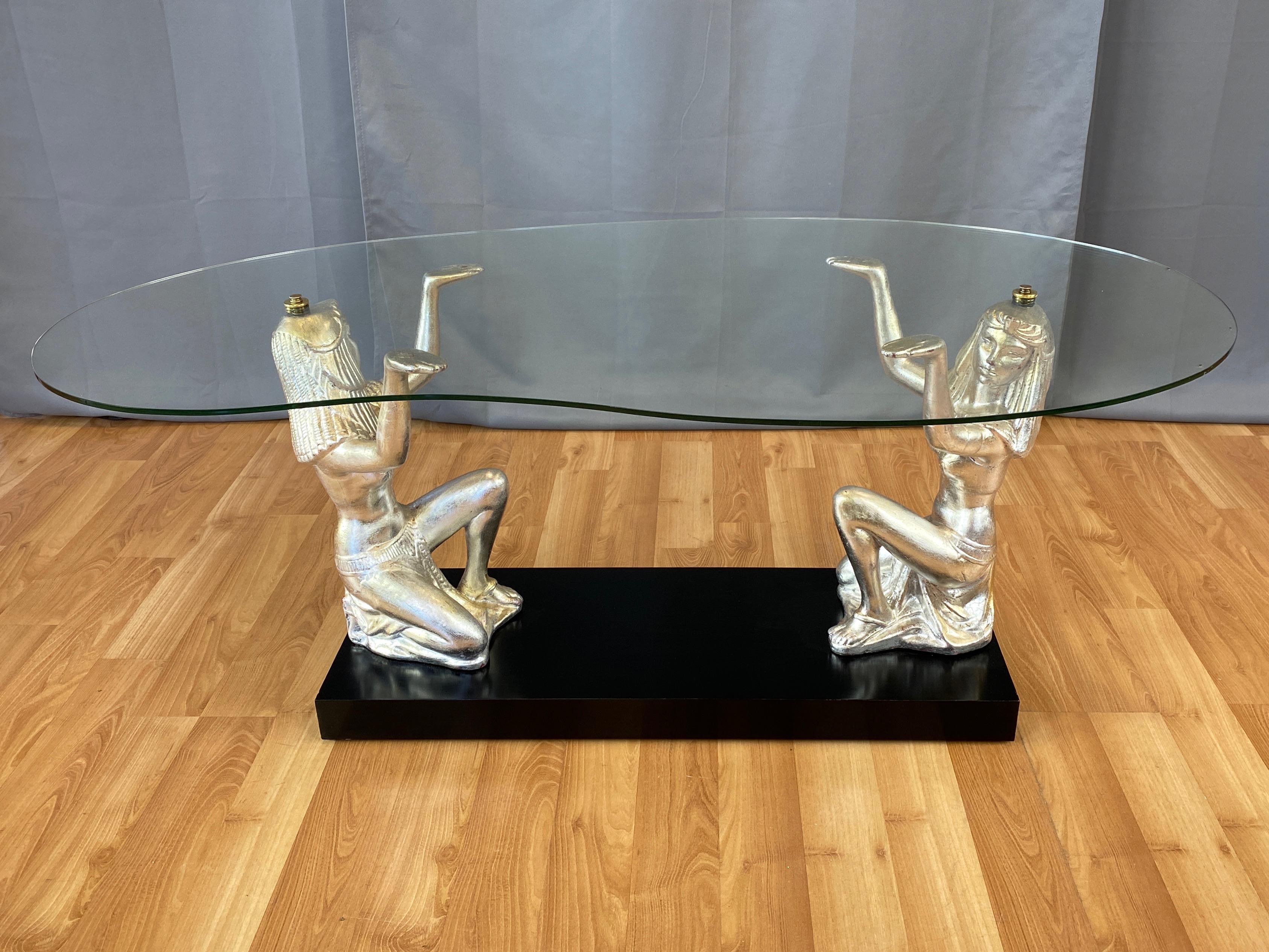 A very uncommon and uniquely stylish 1951 Egyptian Revival-inspired Hollywood Regency figural glass top coffee table by California Lamps & Shades Company.

Free-form glass top held regally aloft by a strikingly beautiful and sculptural pair of lithe