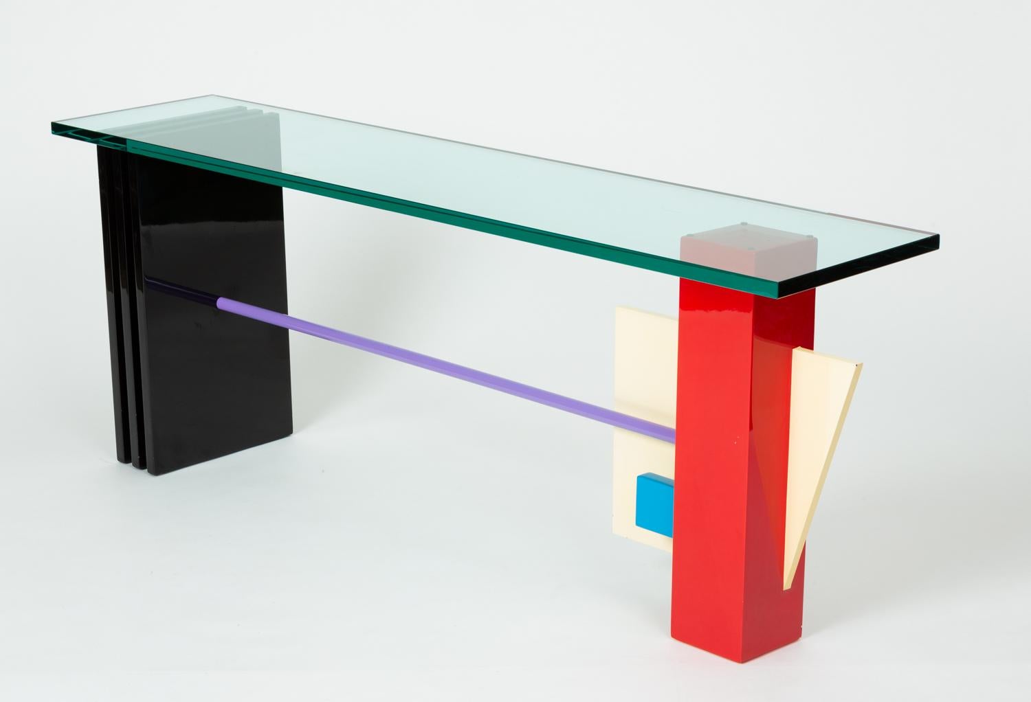 Bold geometry and colors are at work in this 1980s Peter Shire-esque console table. A thick glass slab perches on top of two mismatched columns, joined by a whimsical lavender-painted dowel support. One column has a vertical slat construction in
