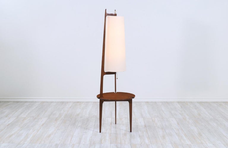 Elegant Mid-Century Modern floor lamp designed by Modeline and manufactured in the United States circa 1960s. This tall floor lamp features a carved and sturdy walnut wood frame with warm grain details that blend smoothly with the newly polished