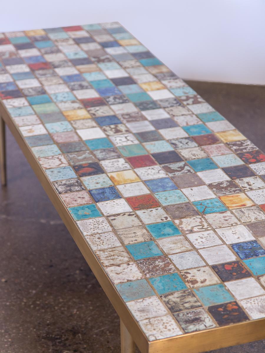 California Modern tile-top brass coffee table. Bright tile-top surface consists of multicolored glazed tiles in different finishes and applications, creating a brilliant mosaic surface. Tiles measure 2.25” and are tightly gridded. The handsome brass