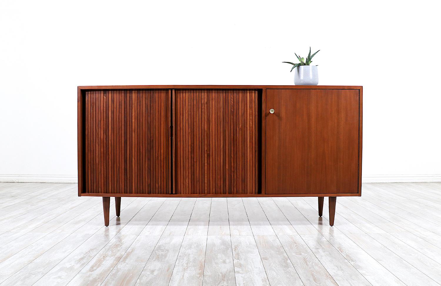 Mid Century Modern Credenza designed by Milo Baughman for Glenn of California in the United States circa 1950’s. Supported by tapered legs and crafted with a walnut frame and two tambour doors that smoothly glide open to reveal a spacious shelved