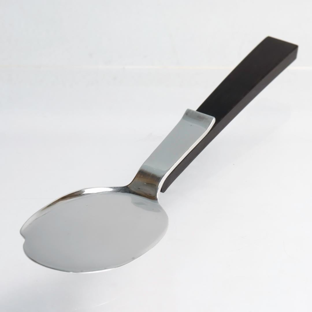 A fine sterling silver & ebony wood server.

By Allan Adler.

In the Town & Country pattern.

This flat serving spoon or server has a raised lip to the right hand side and a flat edge to the left with a riveted, tapered ebony handle.

(We're not