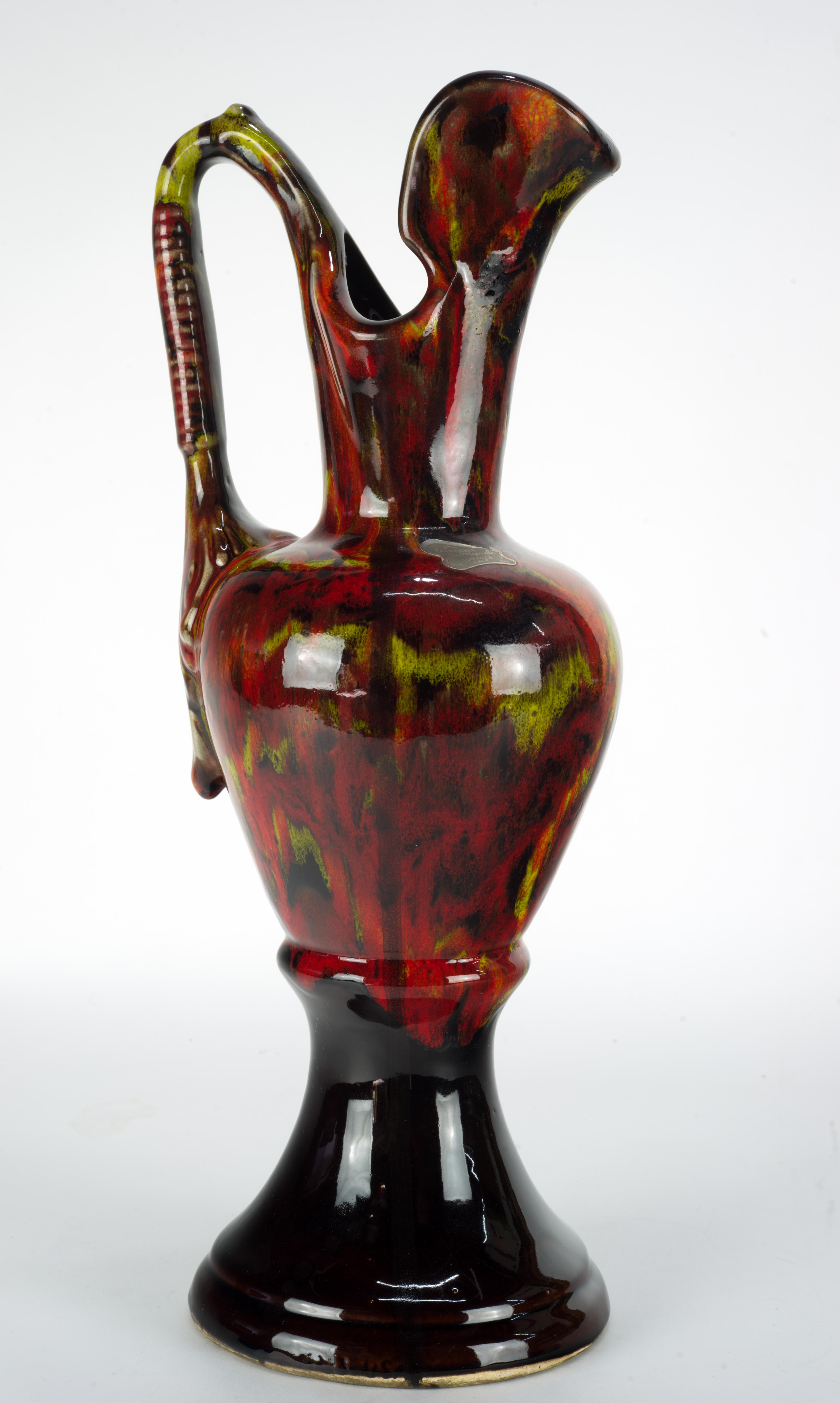  Bright and distinct ewer vase was made by California Originals pottery in 1950s-1960s. It is decorated with intense multicolored drip glaze in red and yellow palette on black background; monochromatic black base contrasts and intensifies the colors