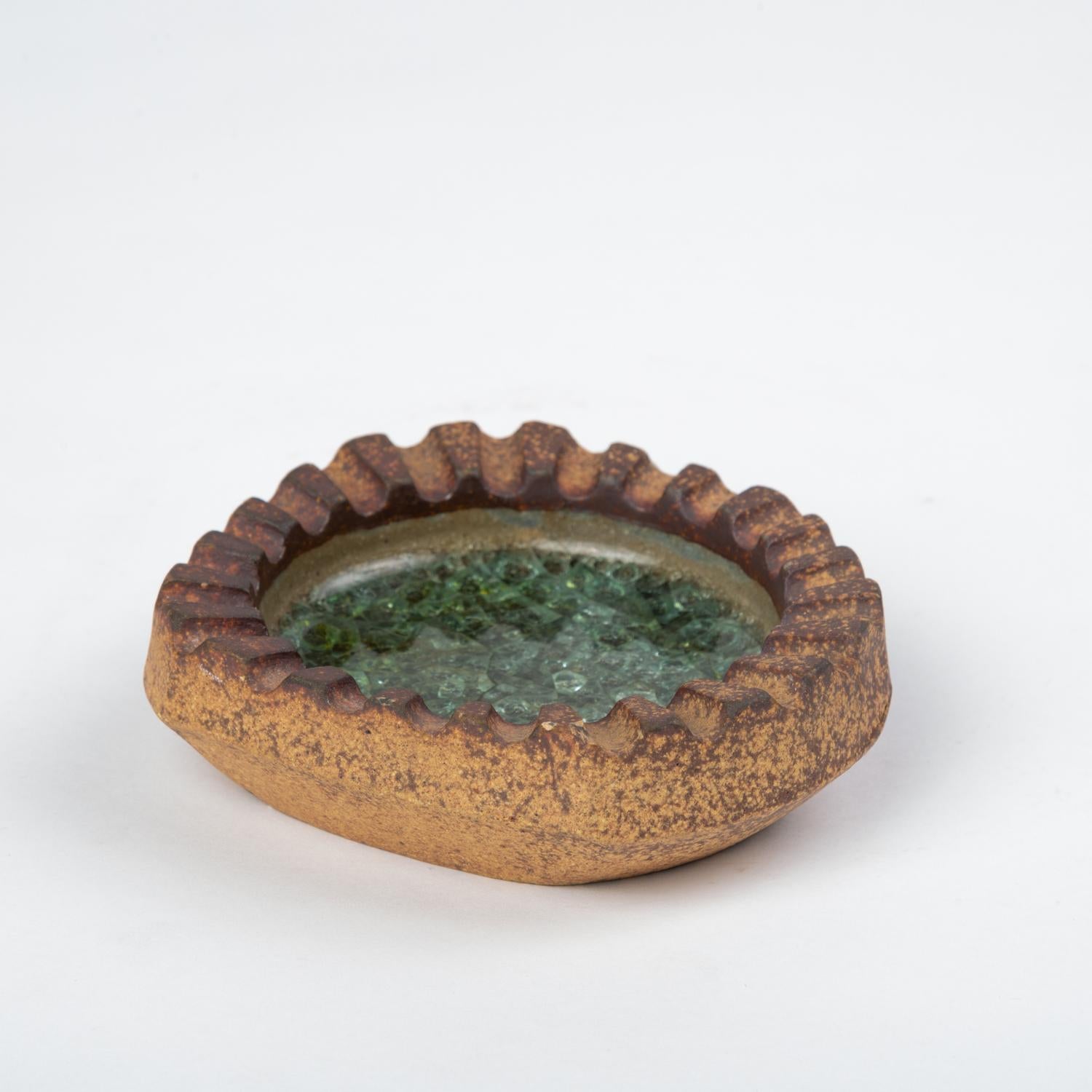 A small stoneware ashtray by renowned California art ceramicist Robert Maxwell with an irregular, crenellated edge and distinctive glazework. The body of the piece is unfinished stoneware, with layered glaze around the interior. The bottom of the