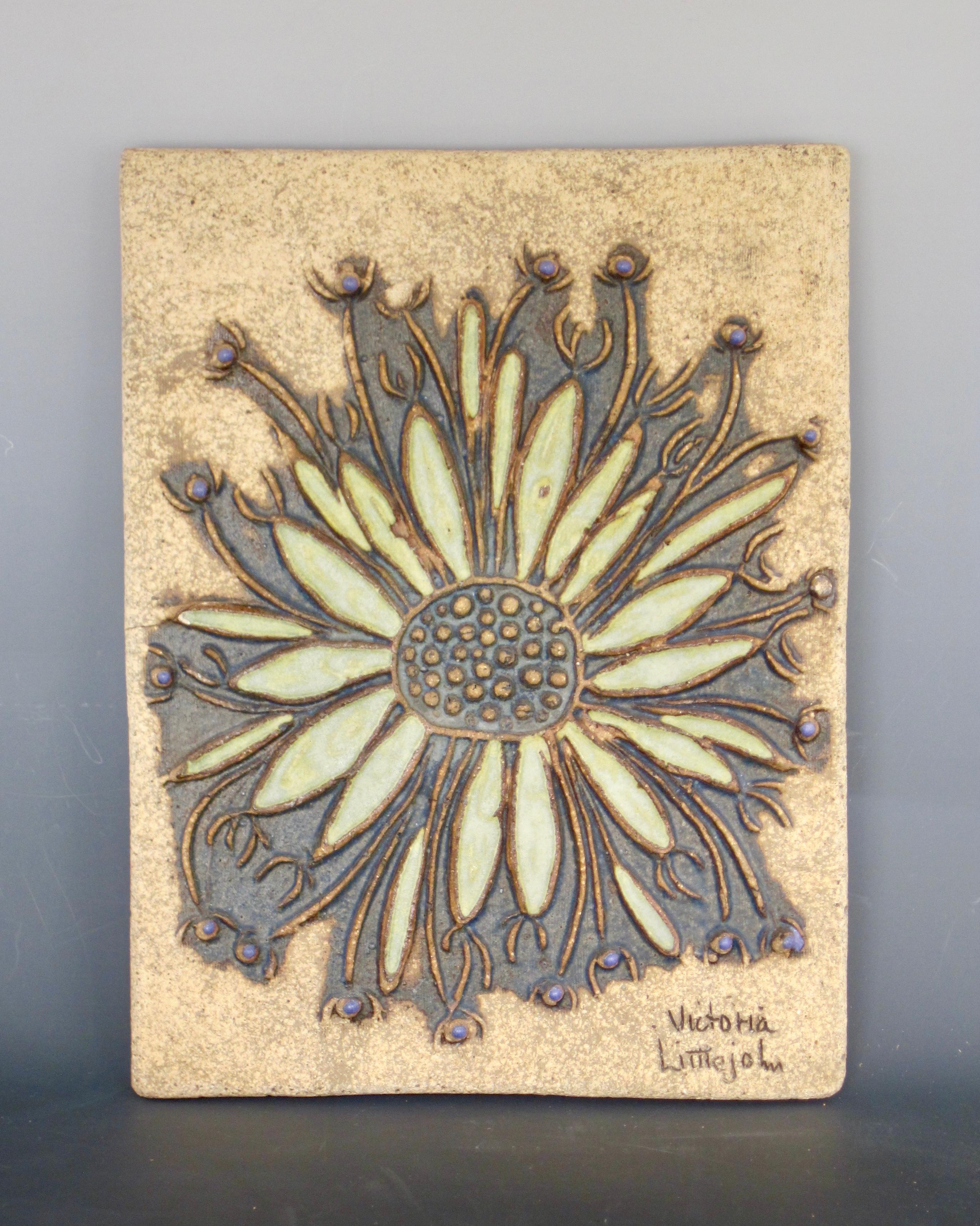 1960s Victoria Littlejohn Studio pottery flower sculpture. A 3 dimensional surface with outlines of the leaves and pistil in the center as well as the the grassy pieces with pods. Pressed board on the reverse with two hooks for hanging.