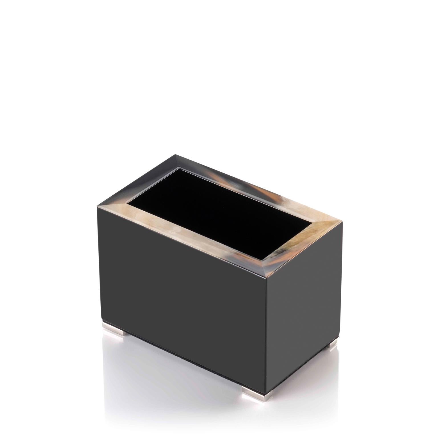 Unser Stifthalter Calipso ist eine elegante Ergänzung für den Schreibtisch. Er hat eine rechteckige Silhouette aus glänzend schwarz lackiertem Holz, die mit einem markanten Rand aus Corno Italiano akzentuiert ist, dessen einzigartige Maserung für
