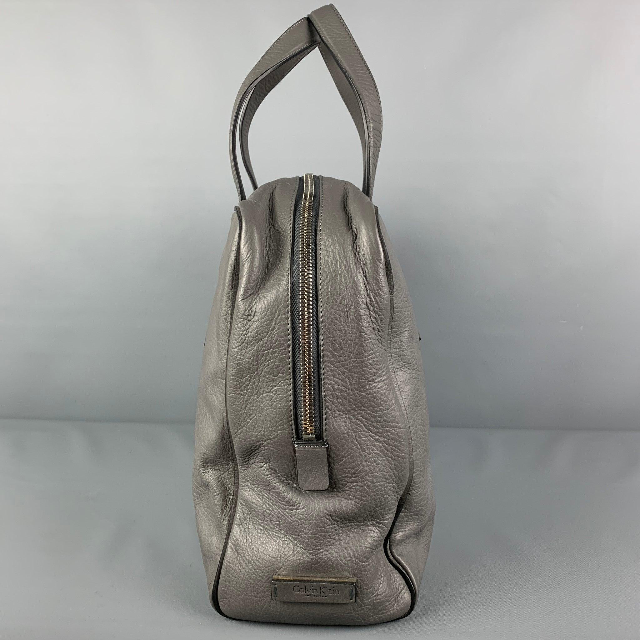 CALVIN KLEIN COLLECTION bag comes in a grey leather featuring top handles, inner slots, silver tone hardware, and a top zipper closure.
New With Tags. 

Measurements: 
  Length: 15.5 inches  Width: 4 inches  Height: 12.5 inches  Drop: 8 inches 
  
 