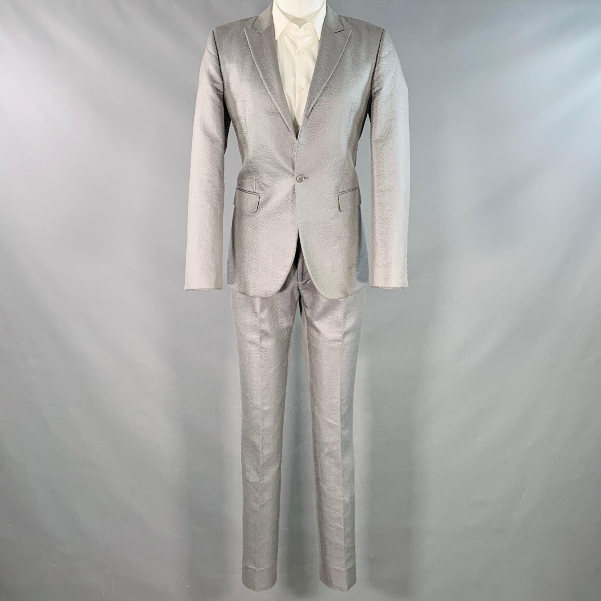 CALVIN KLEIN COLLECTION Costume
en coton mélangé gris métallisé avec une doublure complète et comprend un manteau de sport à un seul boutonnage avec un revers en pointe et un pantalon à devant plat assorti. Fabriqué en République tchèque. Très bon