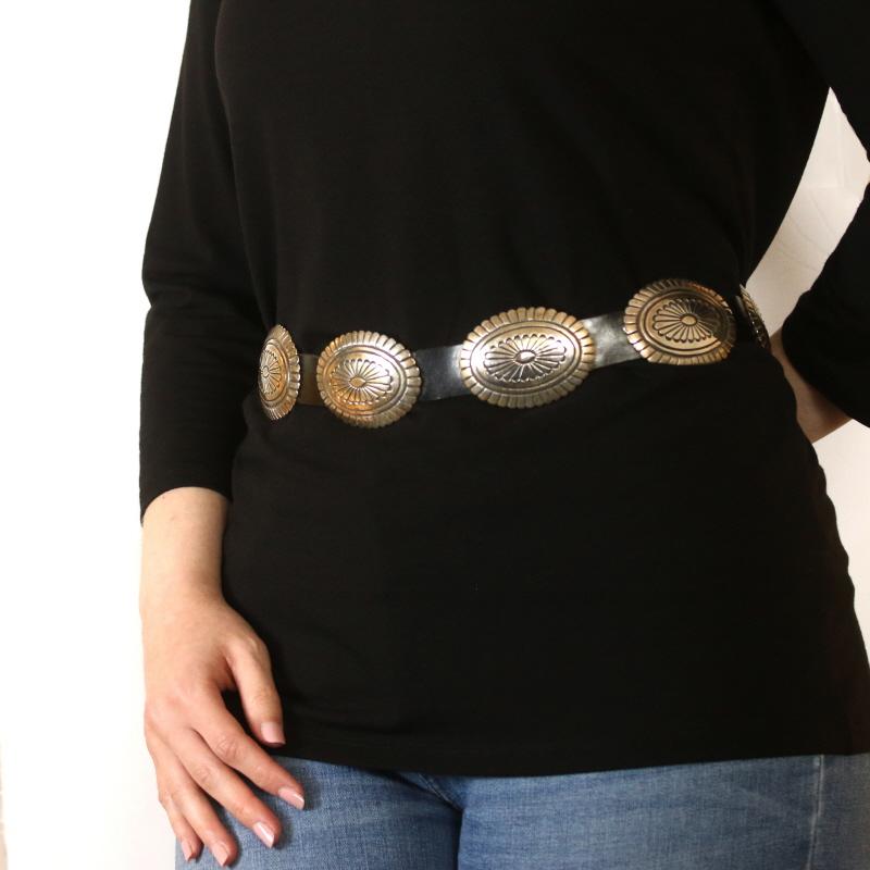 This Navajo belt would make a wonderful addition to a collection of First Nations art. Crafted by Calvin Maloney in sterling silver, the belt features ten matching conchas threaded onto a black leather band. Desert flowers and feather designs