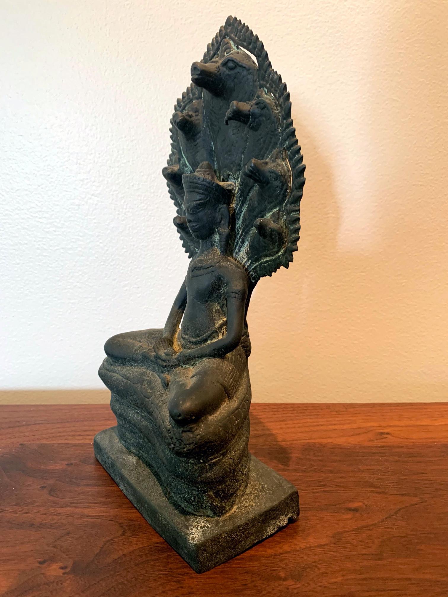 A cast bronze statue of Buddha in deep mediation on a throne and canopy formed by Mucalinda Naga, a multi-head serpent like creature. The statue depicts the legend that four weeks after Gautama Buddha began meditating under the Bodhi Tree, the