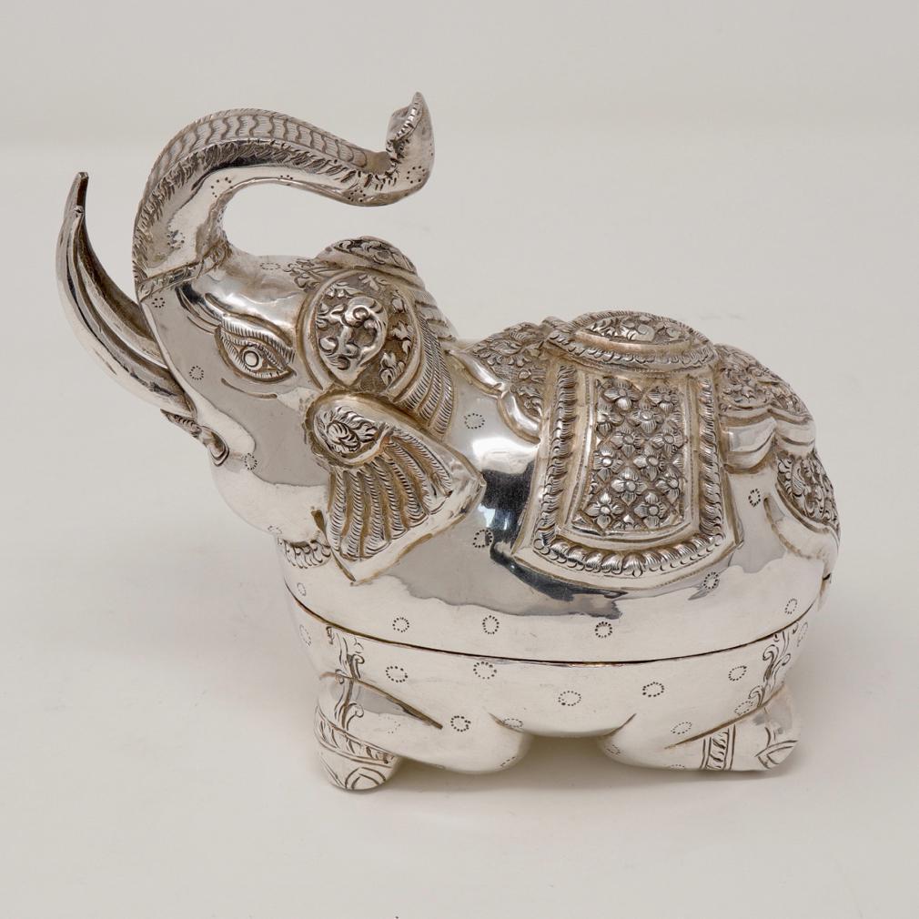 Cambodian Silver Elephant Box. A traditional sturdy crouching elephant form with front legs tucked beneath him and the hind kneeling underneath. The hammered silver  with caparisoned saddle blanket on the spotted body with tusks and trunk pointed