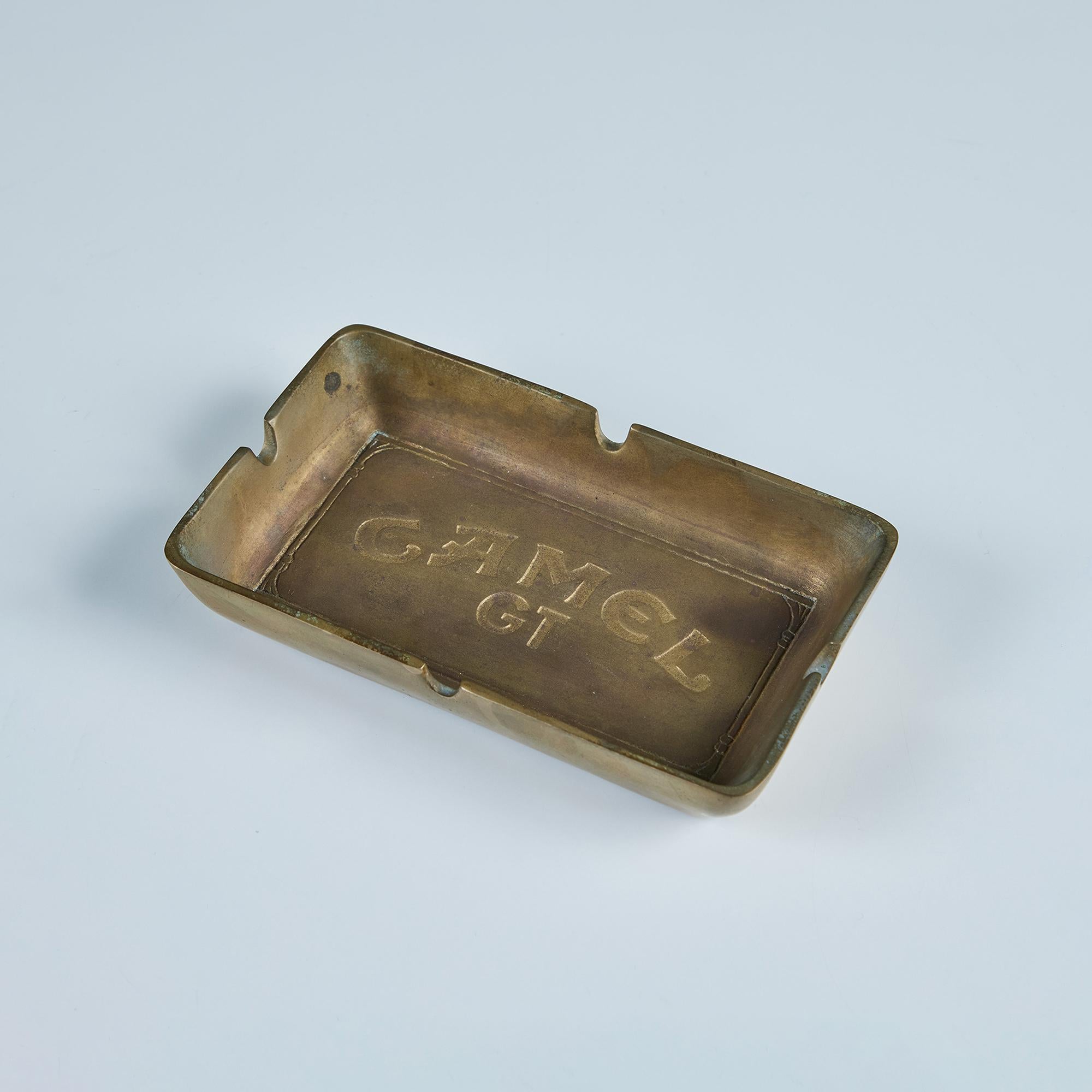Cast brass ashtray c.1984 by R.J. Reynolds Tobacco Co. features the Camel Logo on the plate of the ashtray. The rectangular dish has high sides with a divot on each side for a cigarette or other smokable items. A playful accessory for a smoking