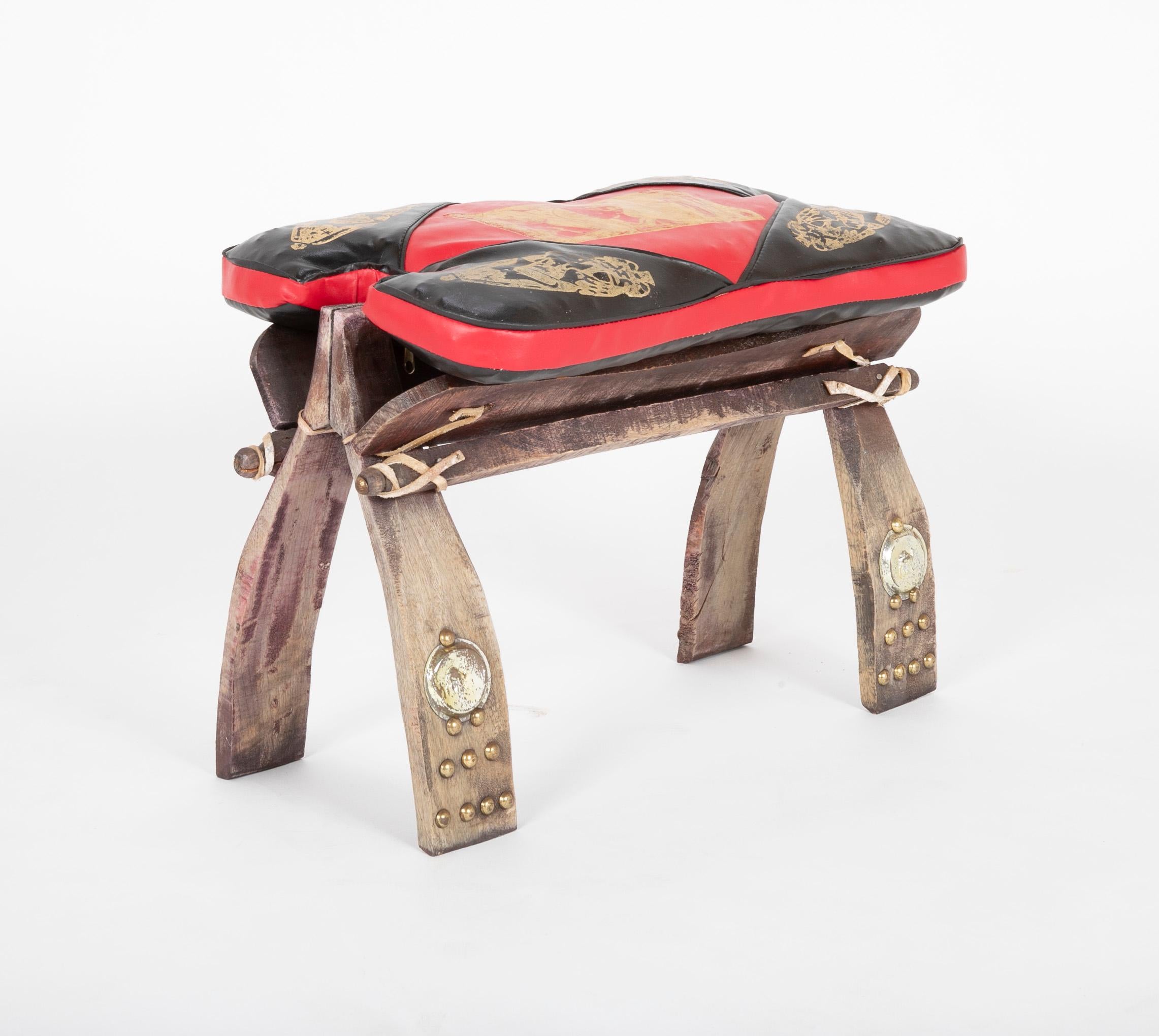 Beautifully aged leather foot stool in the form of a camel seat having brass accents.