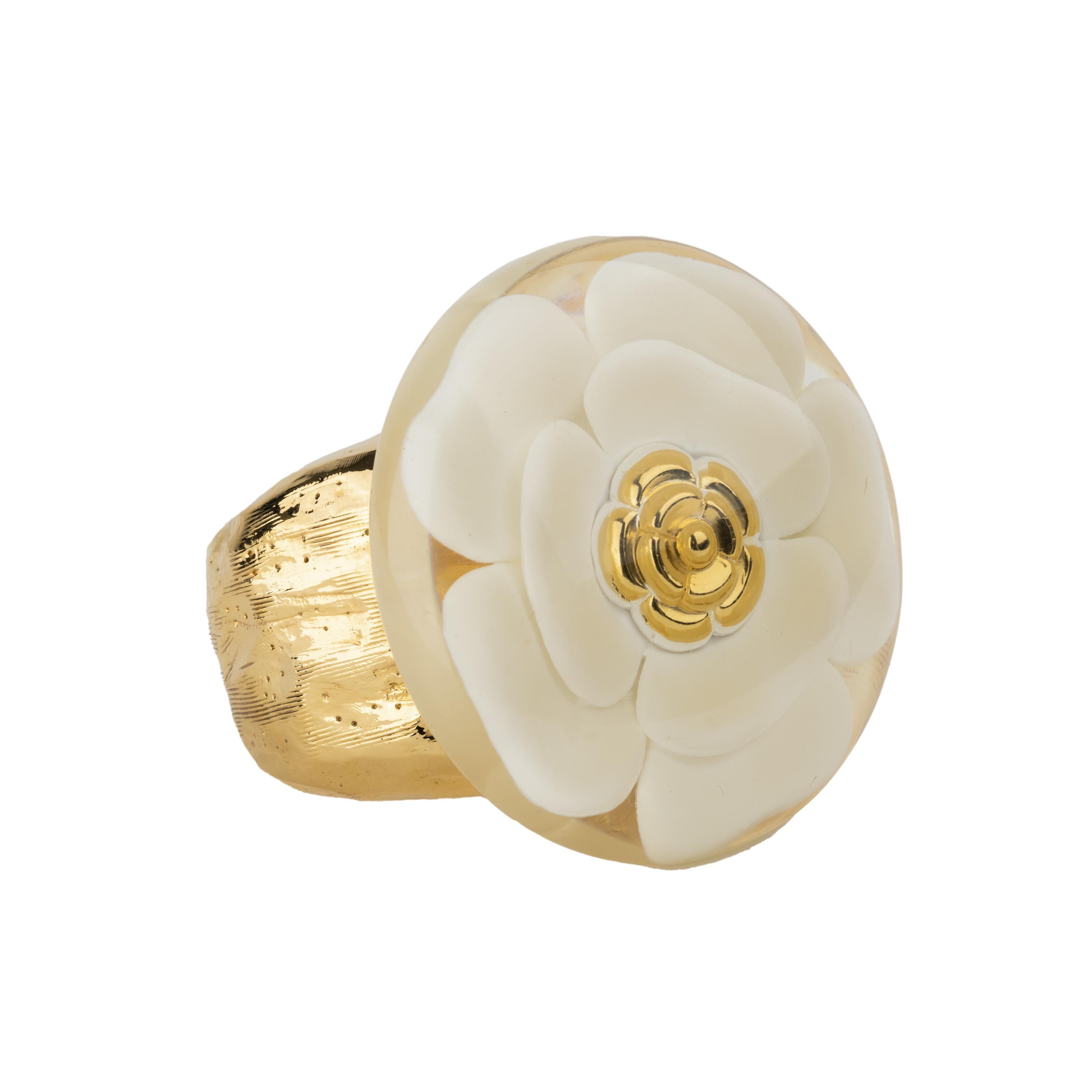 Chanel gold-plated metal bracelet. Open rigid style, decorated with the famous fashion house's symbol: the white camellia, placed inside a disc in transparent glossy acrylic.

NFT option available.
