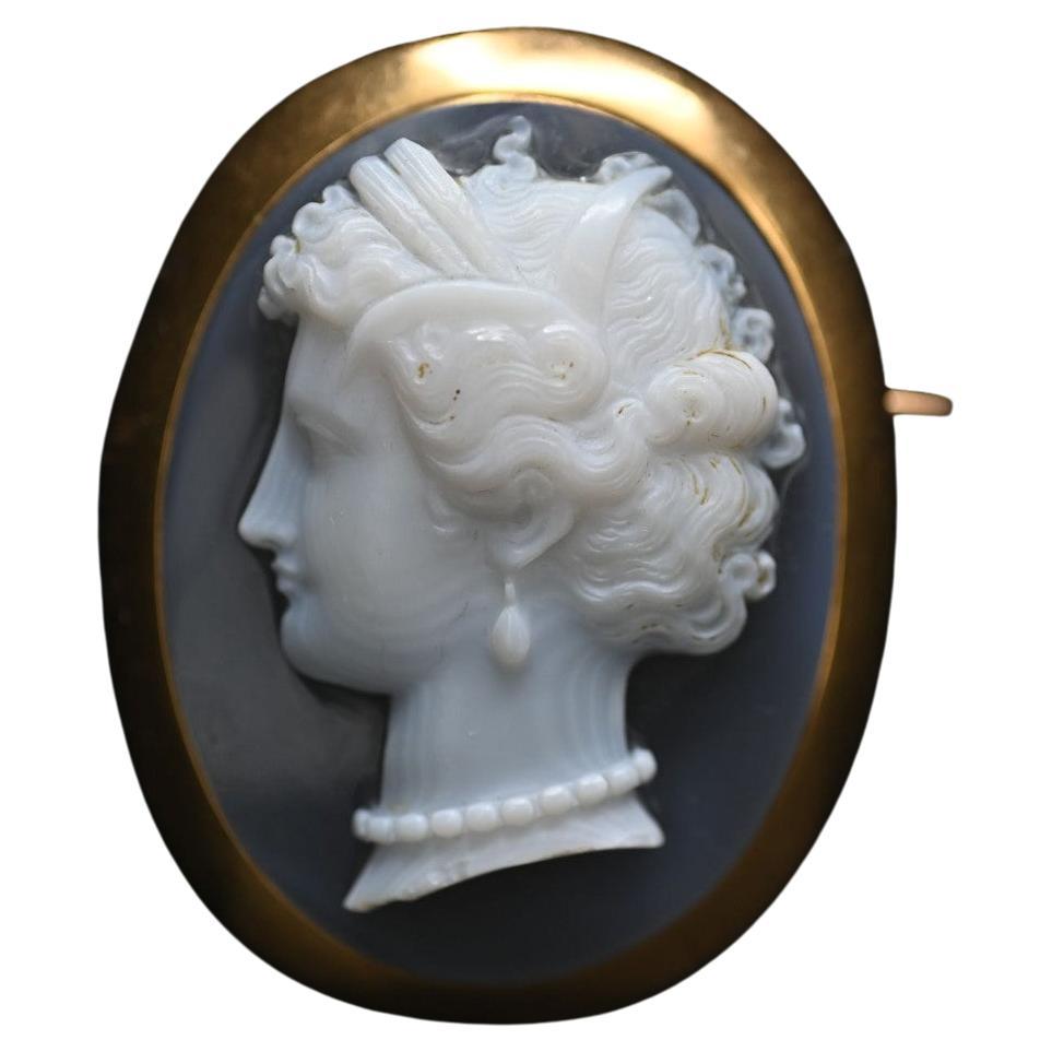Broche centrée d'un camée sur agate bleutée ornée d'un profil de femme portant des bijoux en perles. Cadre en or 18K Avec son étui d'origine. Bon état. Poids brut : 35,3 g
Taille 52mm x 42mm