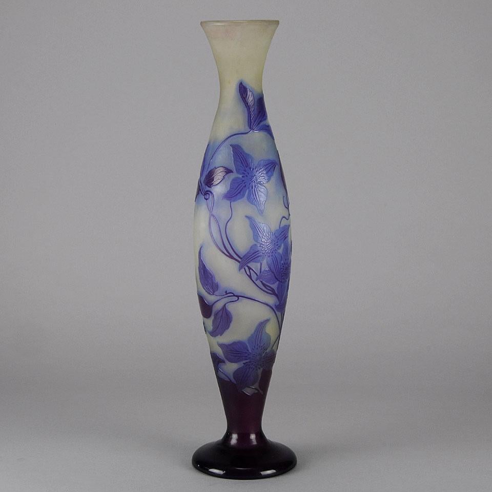 A very fine tall slender glass vase decorated with an Art Nouveau Clematis floral design in blue and purple against a pale white field, exhibiting excellent color and good detail. Signed Gallé