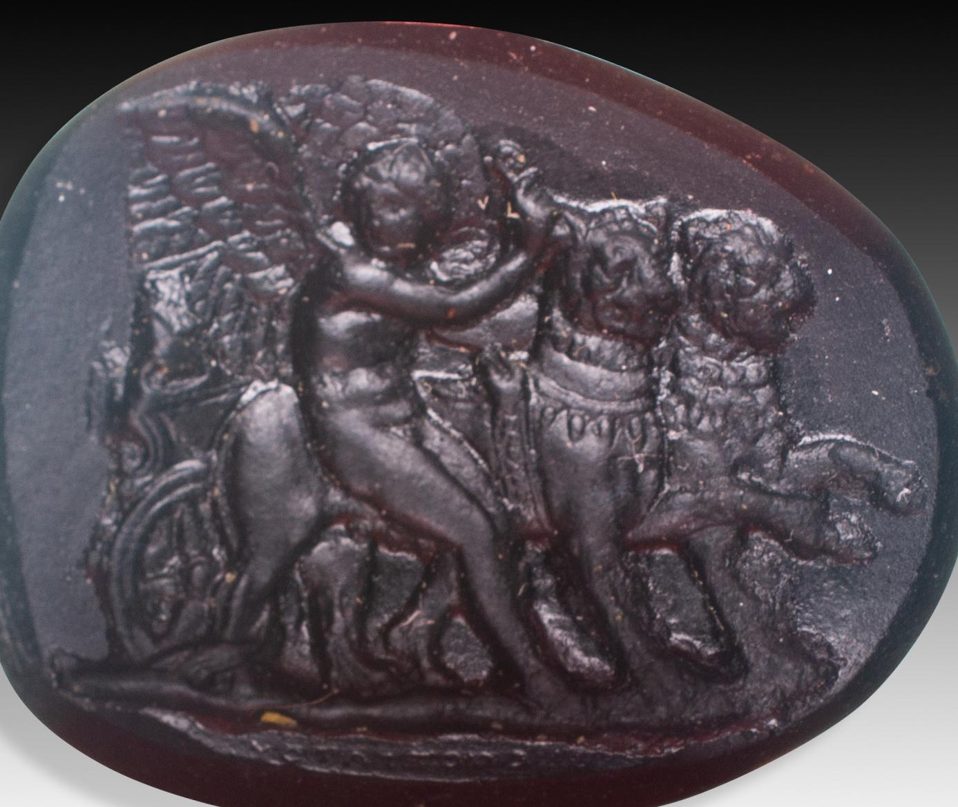 Cameo or intaglio, Cupid guiding lions. Glass. Possibly, Italy, 19th century. 
You can see, in the foreground, a naked and winged child figure, Cupid (or Eros, god of love), guiding two lions, which pull a chariot (note the wheel). These scenes were