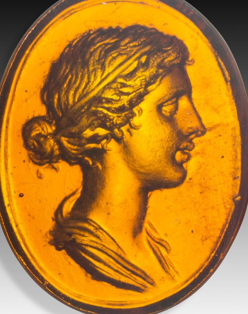  Cameo or intaglio, Lady. Glass. Possibly Italy, 19th century. 
Profile of a woman with her hair gathered in a bun and adorned with a ribbon, following the usual way of representing prominent ladies of Ancient Rome. These types of pieces were