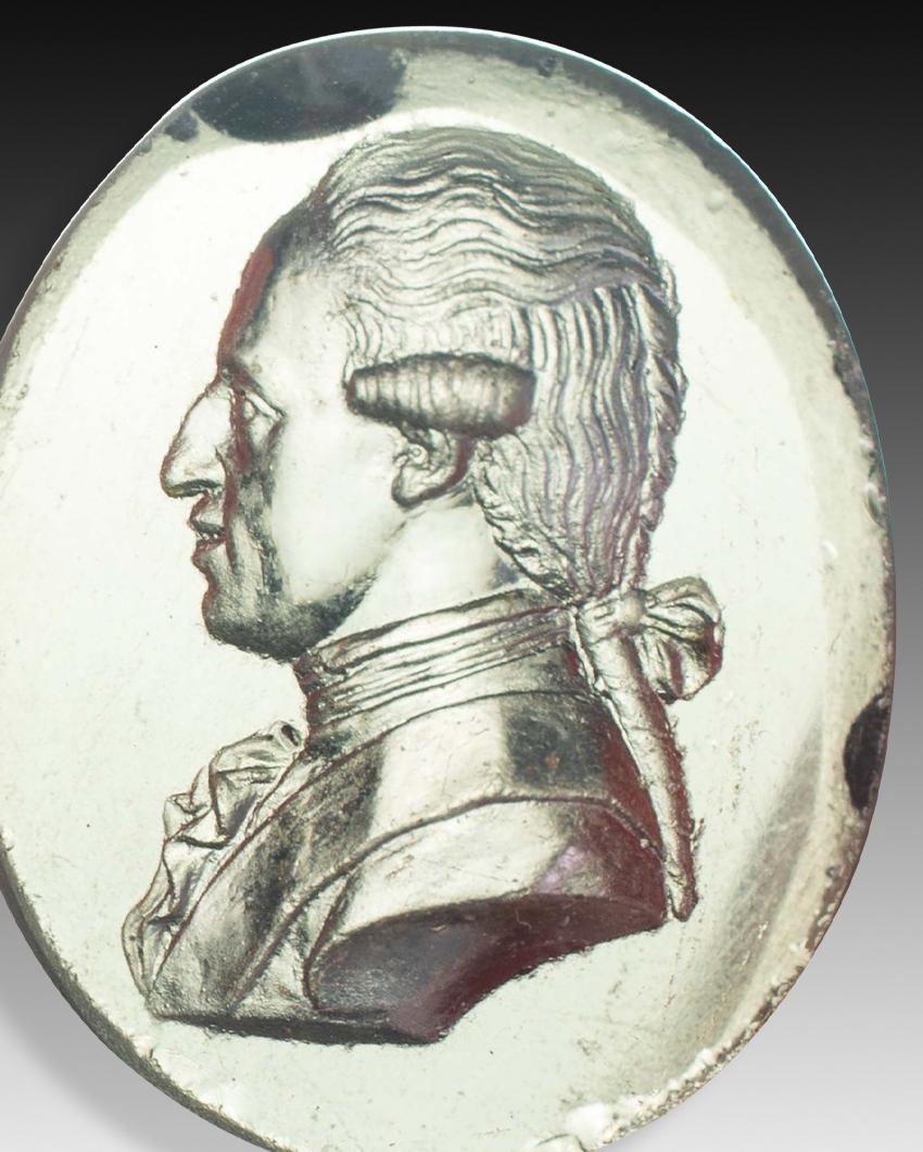 Cameo or intaglio, portrait. Glass. Possibly Spain, 19th century. 
Glass cameo with a profile bust of a male figure with a curly wig and a bow tying a low ponytail. Based on comparisons with other portraits, it is possible that this is of Charles IV
