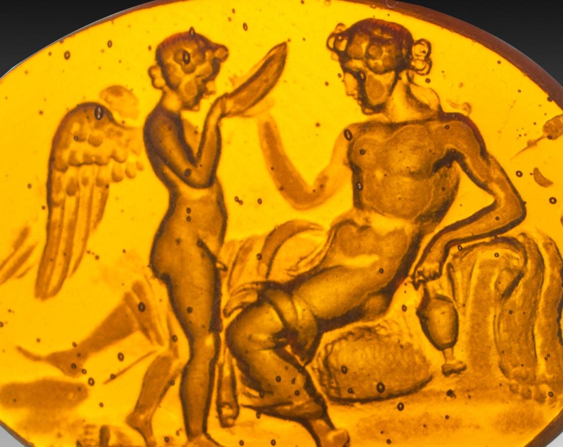  Cameo or intaglio, possibly Venus and Cupid. Glass. Possibly Italy, 19th century.
 A female figure is shown lying down, half-naked, holding a jug or amphora in her hand, while a winged, naked child is seen raising an object to its mouth. This may