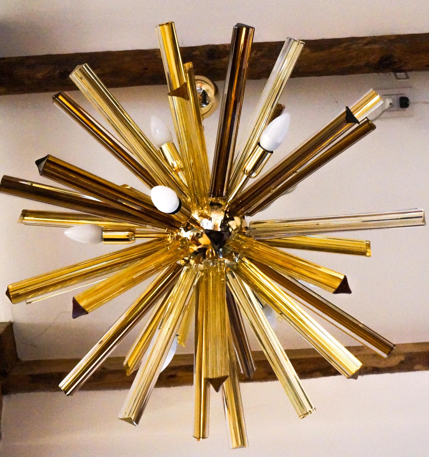 Made up of 41 elements called Trihedrons, this chandelier belongs to that category called sputnik.
The amber color of the glass elements perfectly matches the golden color of the frame. It reaches a diameter of 75 cm and, when turned on, it comes