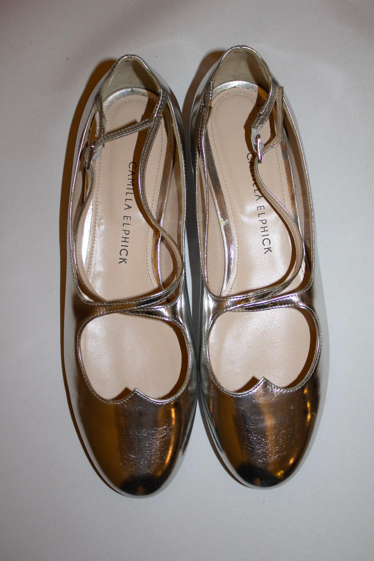A fun  pair of shoes by British designer Camilla Elphick. In silver leather with leather soles, the shoes have an almond shape toe and a cross over front. Size 38 1/2''.
