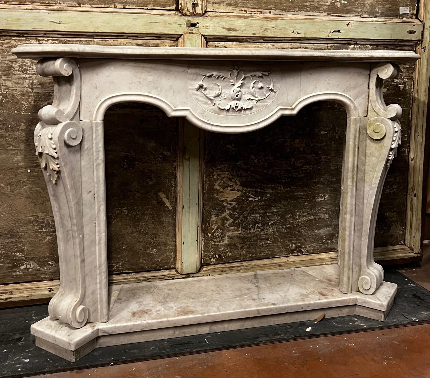 Chimenea antigua de mármol blanco de Carrara. ricamente tallada En la parte delantera, justo debajo de la parte superior de la chimenea hay tallas ornamentales, motivos florales y volutas, que le dan un aspecto refinado y artístico, Los lados