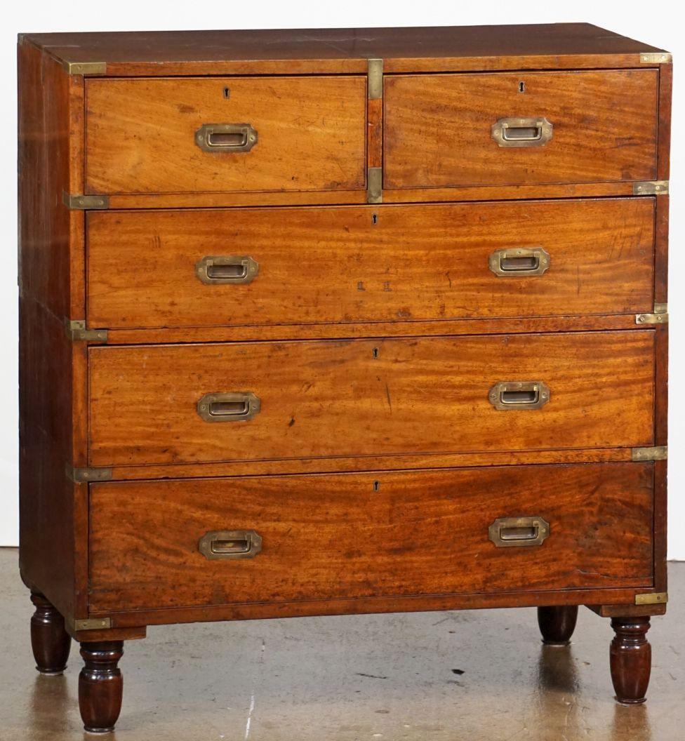 A fine British military officer’s Campaign ware secretary or secretaire from the 19th century, fashioned as a chest of drawers, featuring a patinated mahogany exterior, showing two short drawers over three long drawers. The top right drawer opening