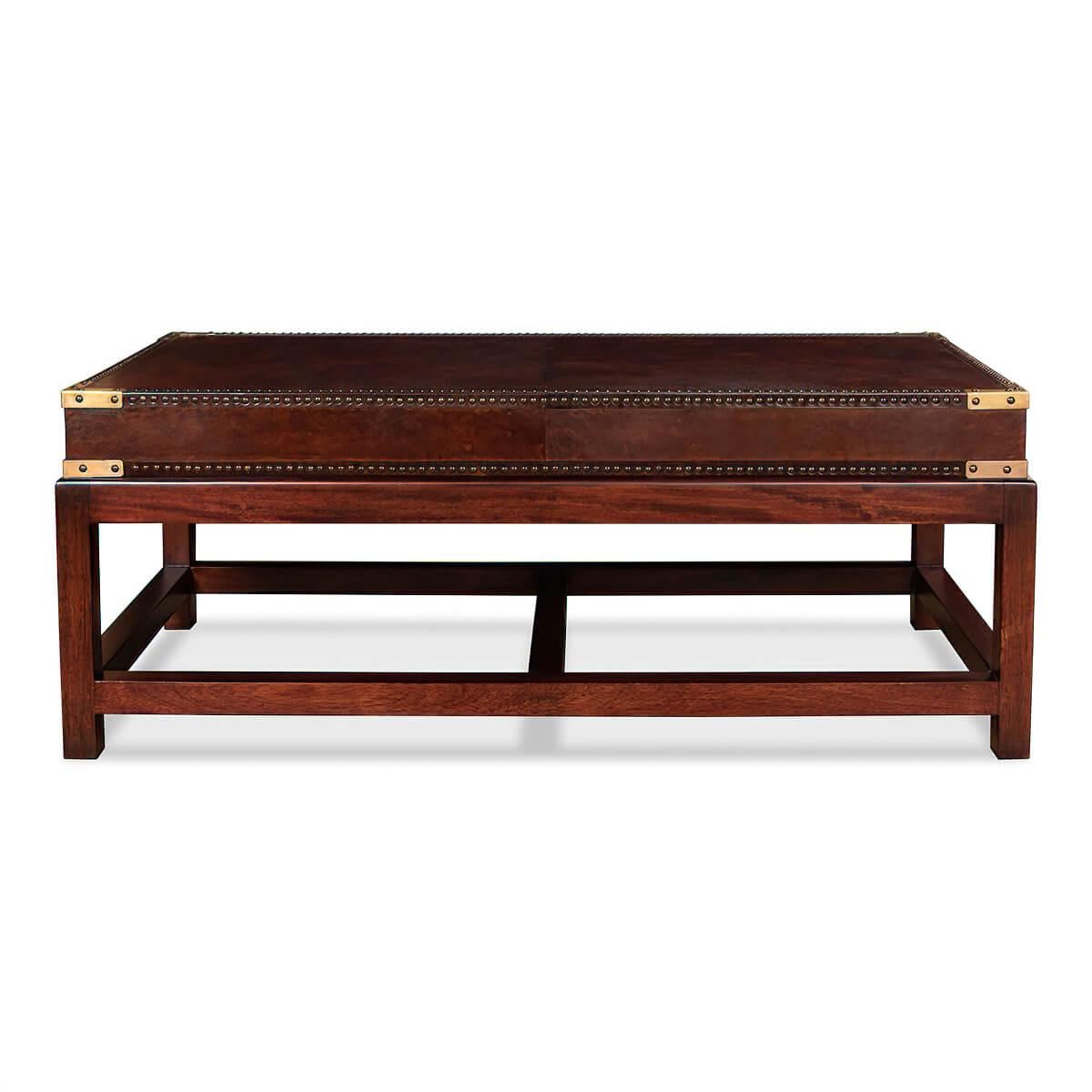 A Campaign form leather wrapped coffee table with an antiqued brown leather, brass-bound corners, and nailhead trim details, raised on a George III style H form stretcher base.

Dimensions
48