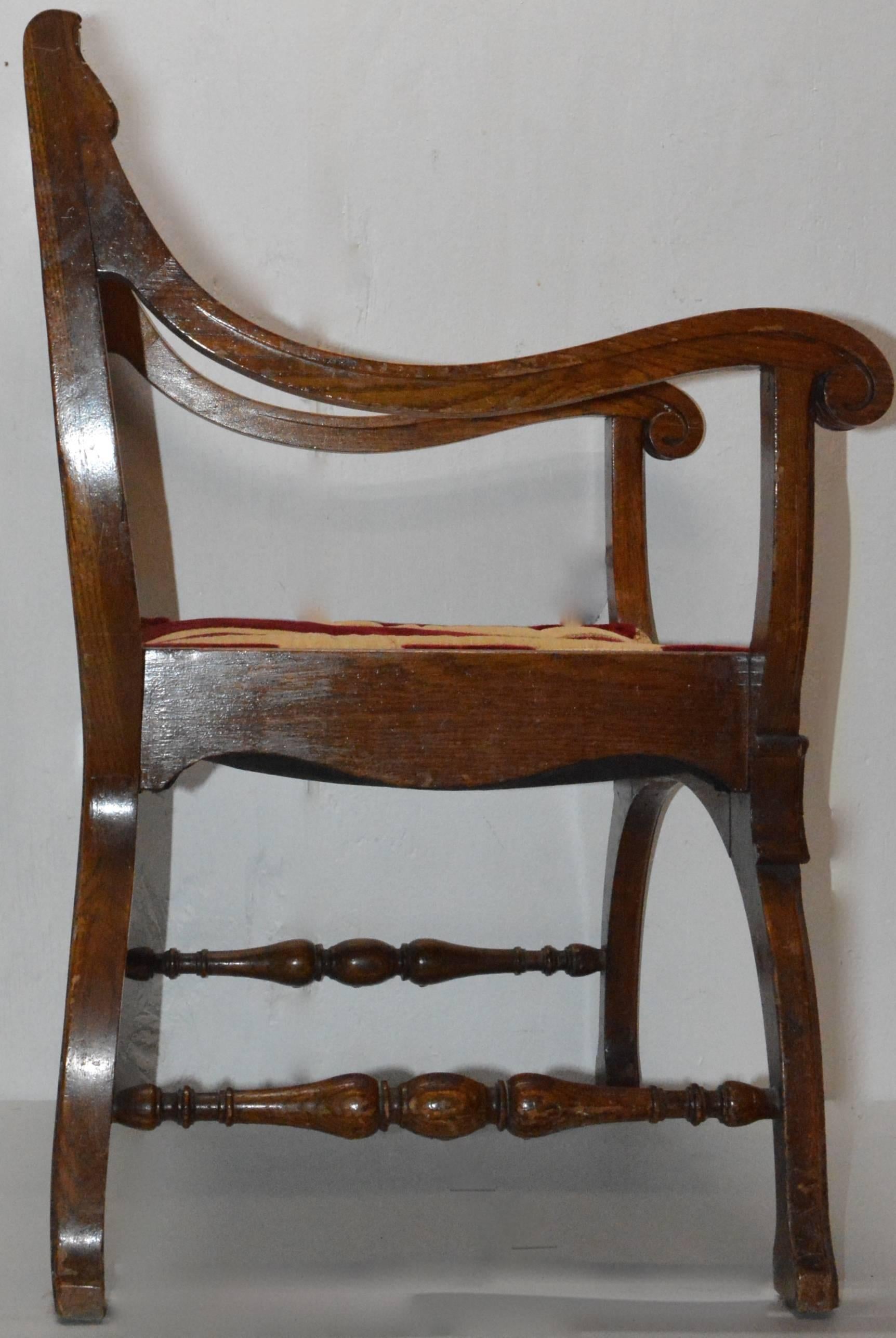 We are offering a wood and fabric chair from the 19th century. It has an intricate inlay design on the back of the chair with lovely scrollwork in the wood. The chair sits on curved legs with turned spindles connecting them. The arms have a ribbed