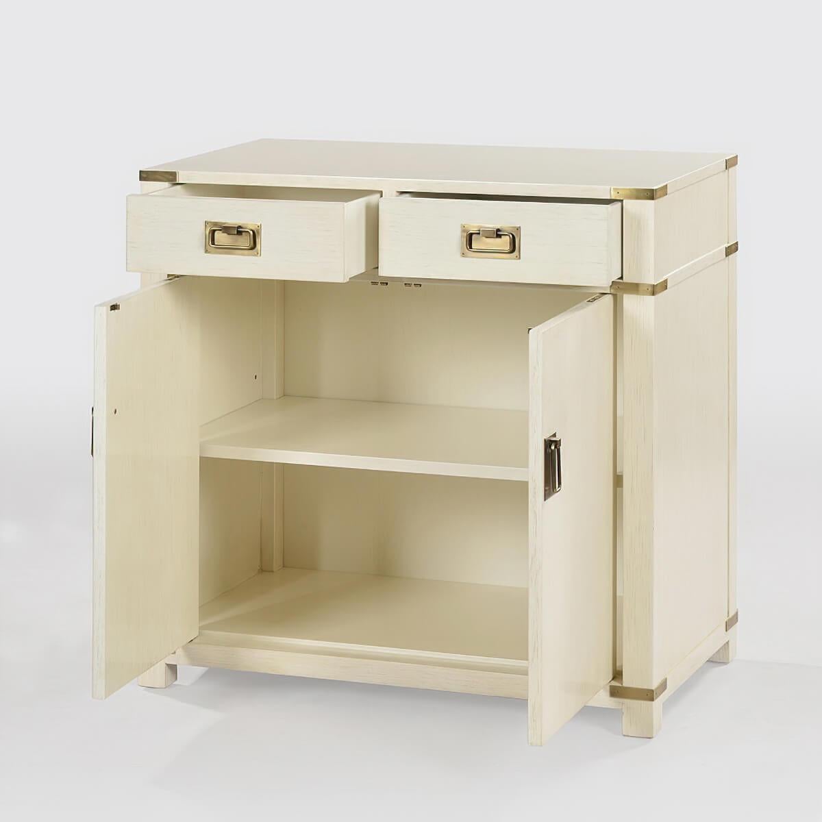 Campaign style cabinet with two drawers, two doors, and hand-cast polished brass hardware has a “drift” white painted finish with subtle grey distressing and hand-rubbed finish.

Dimensions: 32