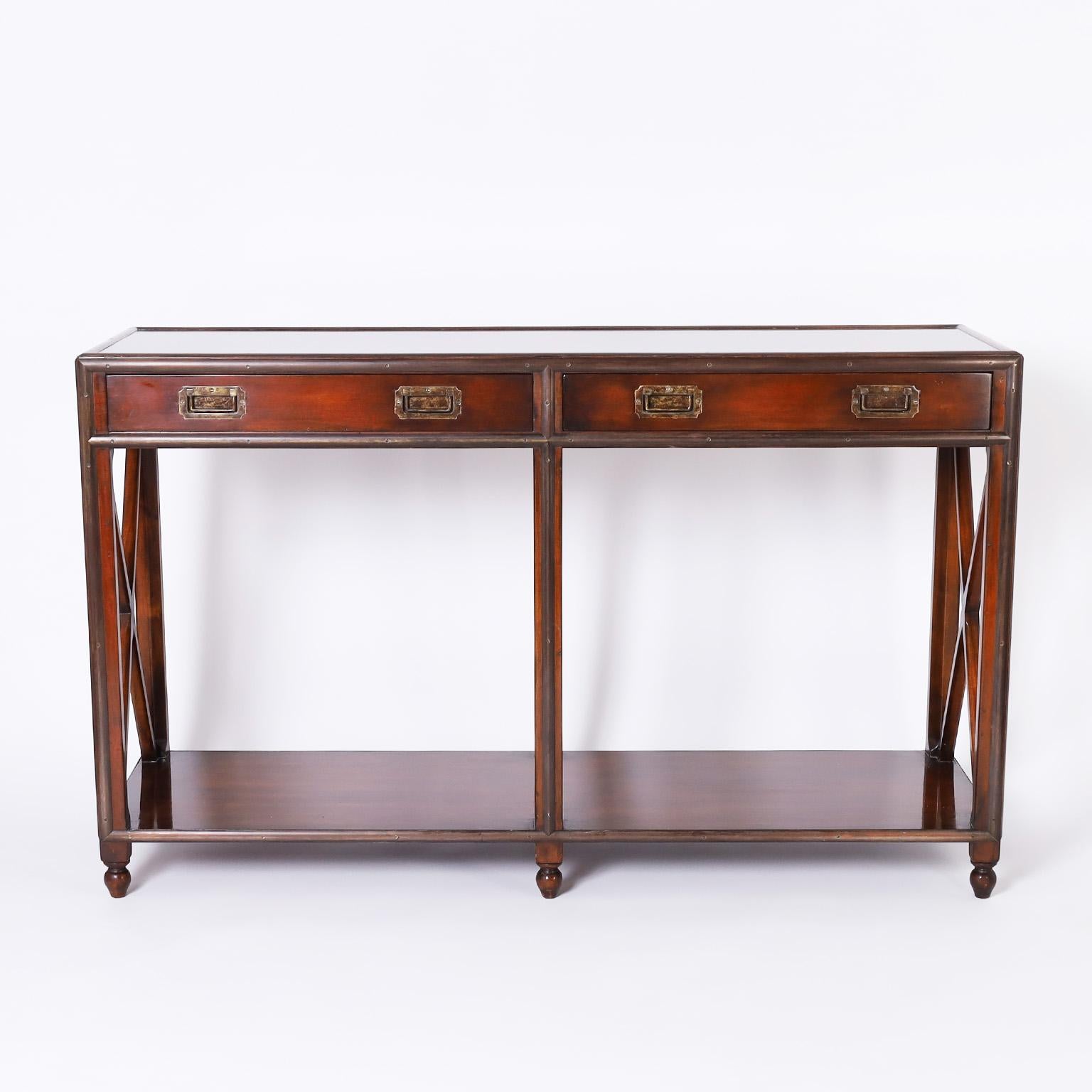 Dashing mid-century two tiered console crafted in mahogany in an unusual form with influences from neoclassic and British colonial. The brass campaign style hardware has a bronze like patina and the piece sits on six turned feet. Attributed to