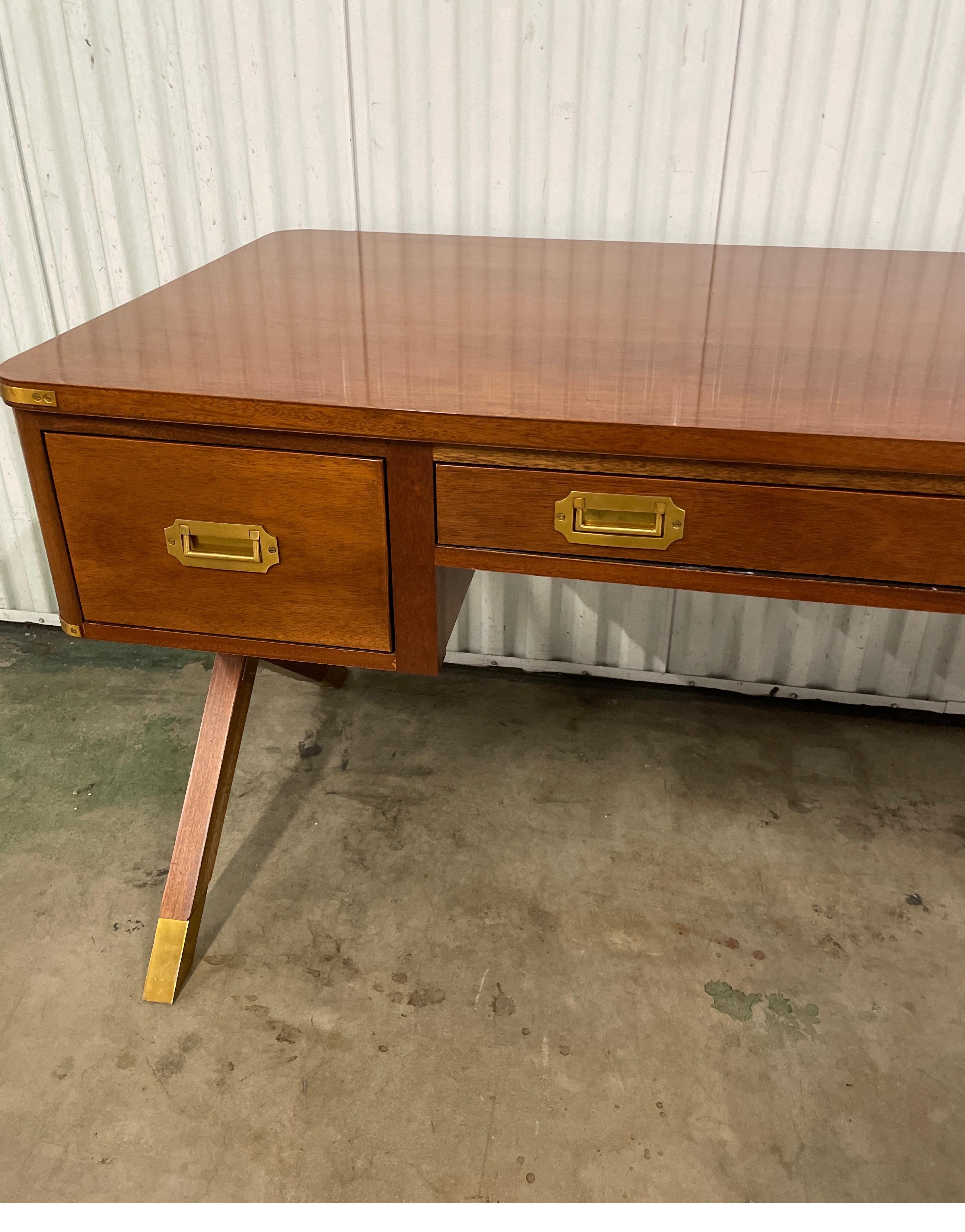 Campaign style desk by Suzanne Kasler for the Hickory Chair Collection. This desk has clean, classic lines. It is a modern take on the traditional campaign pieces. It has X legs & brass hardware. It is finished in a light walnut color. This