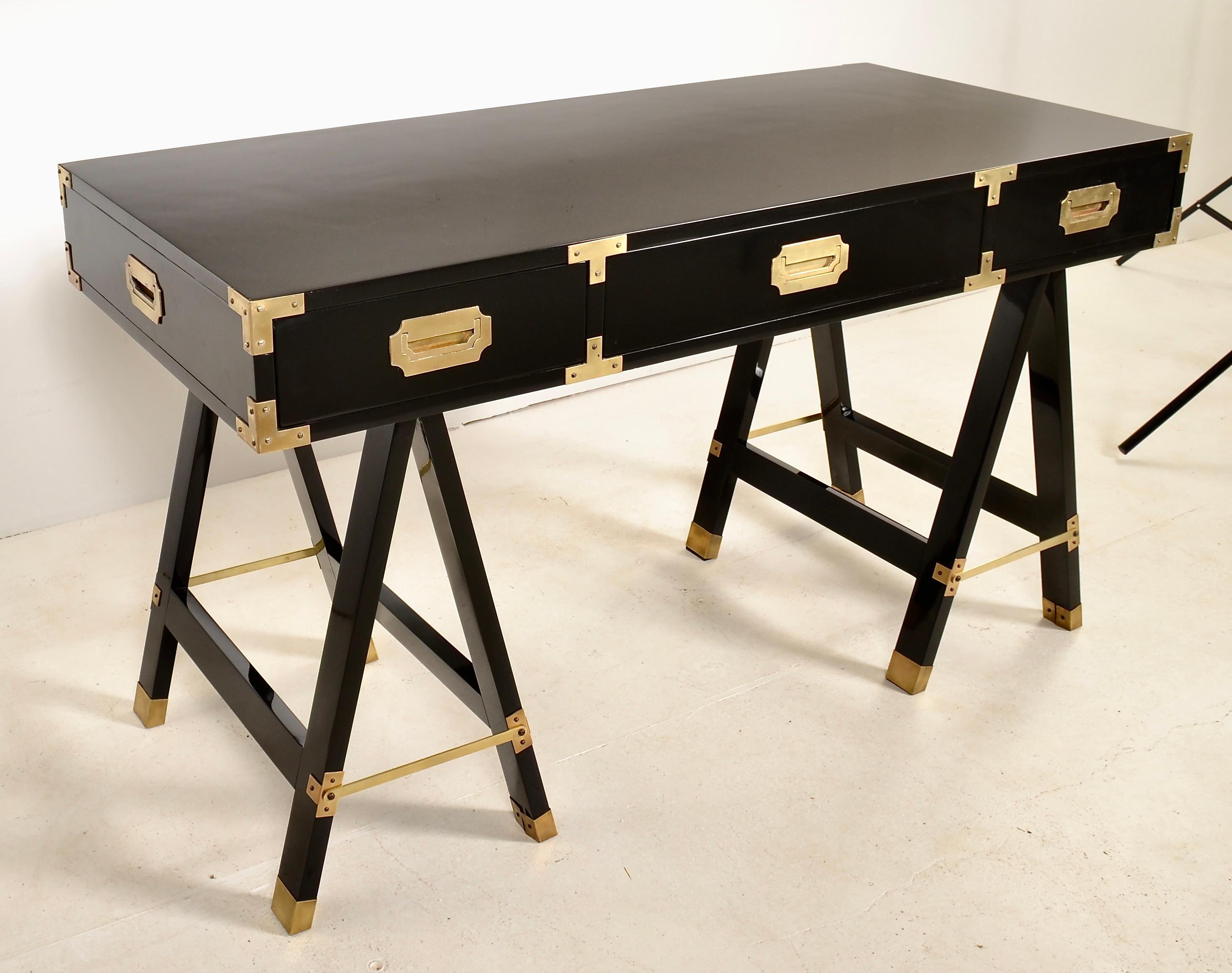 Campaign-style desk on saw horse form supports. Newly lacquered in high gloss black lacquer. Original brass finished hardware. The desk features three drawers, and at 6