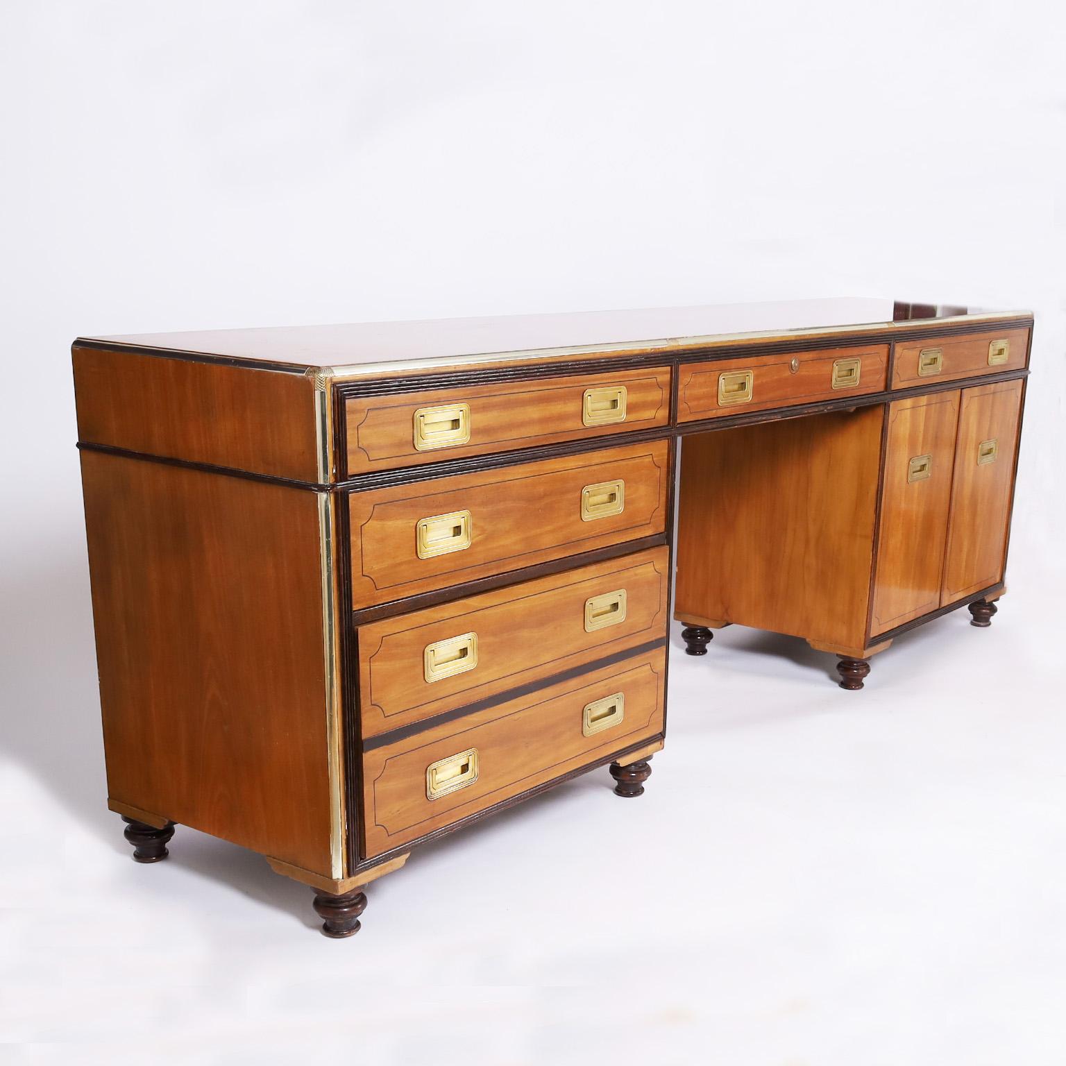 Standout vintage desk or credenza crafted in mahogany and satinwood with multiple components having a wide profile with four drawers on one side and a cabinet with two shelves on the other, campaign style hardware, and turned feet. Signed Baker