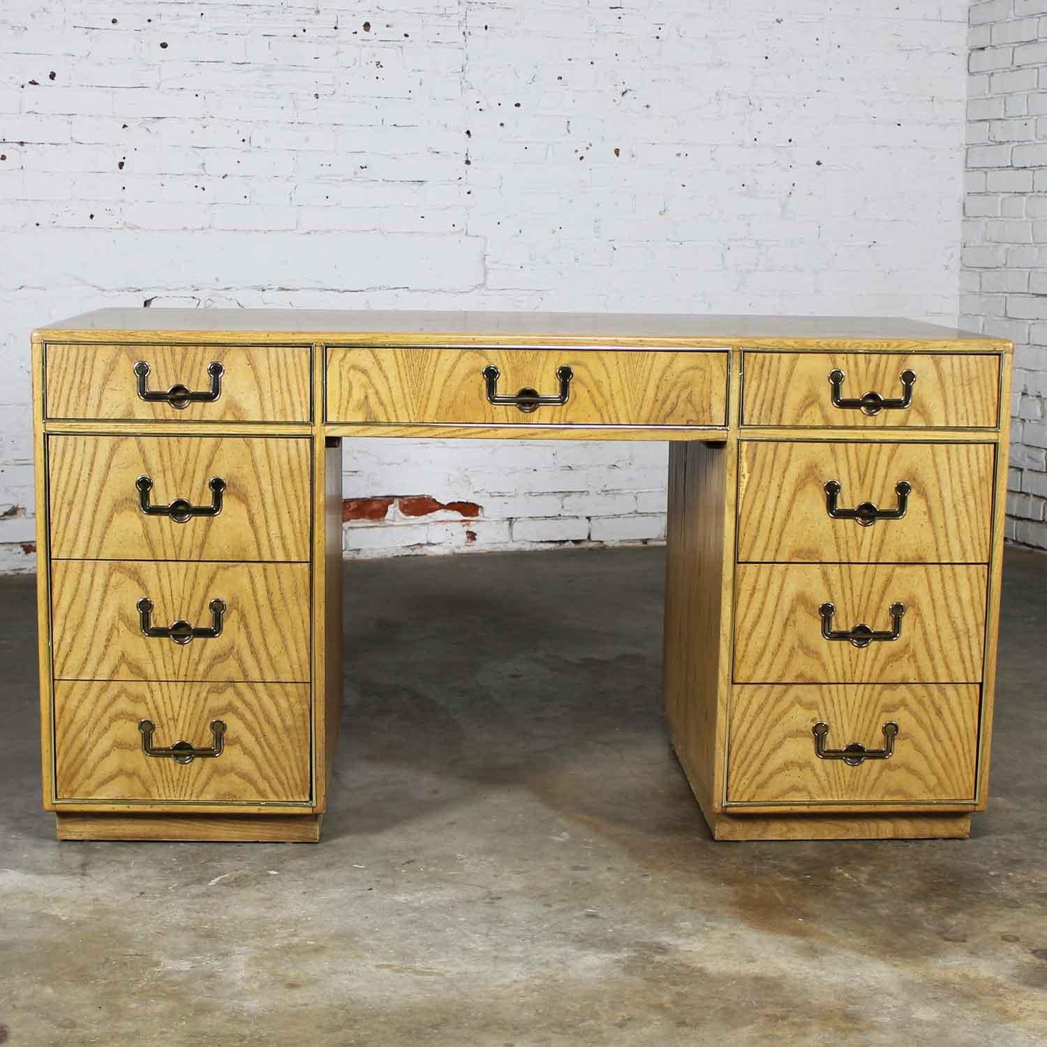 Handsome Campaign style writing desk in light oak bookmatched veneer and brass plate accent and hardware made by Founders Furniture. This piece is in wonderful vintage condition apart from some missing veneer on one of the drawers which has now been